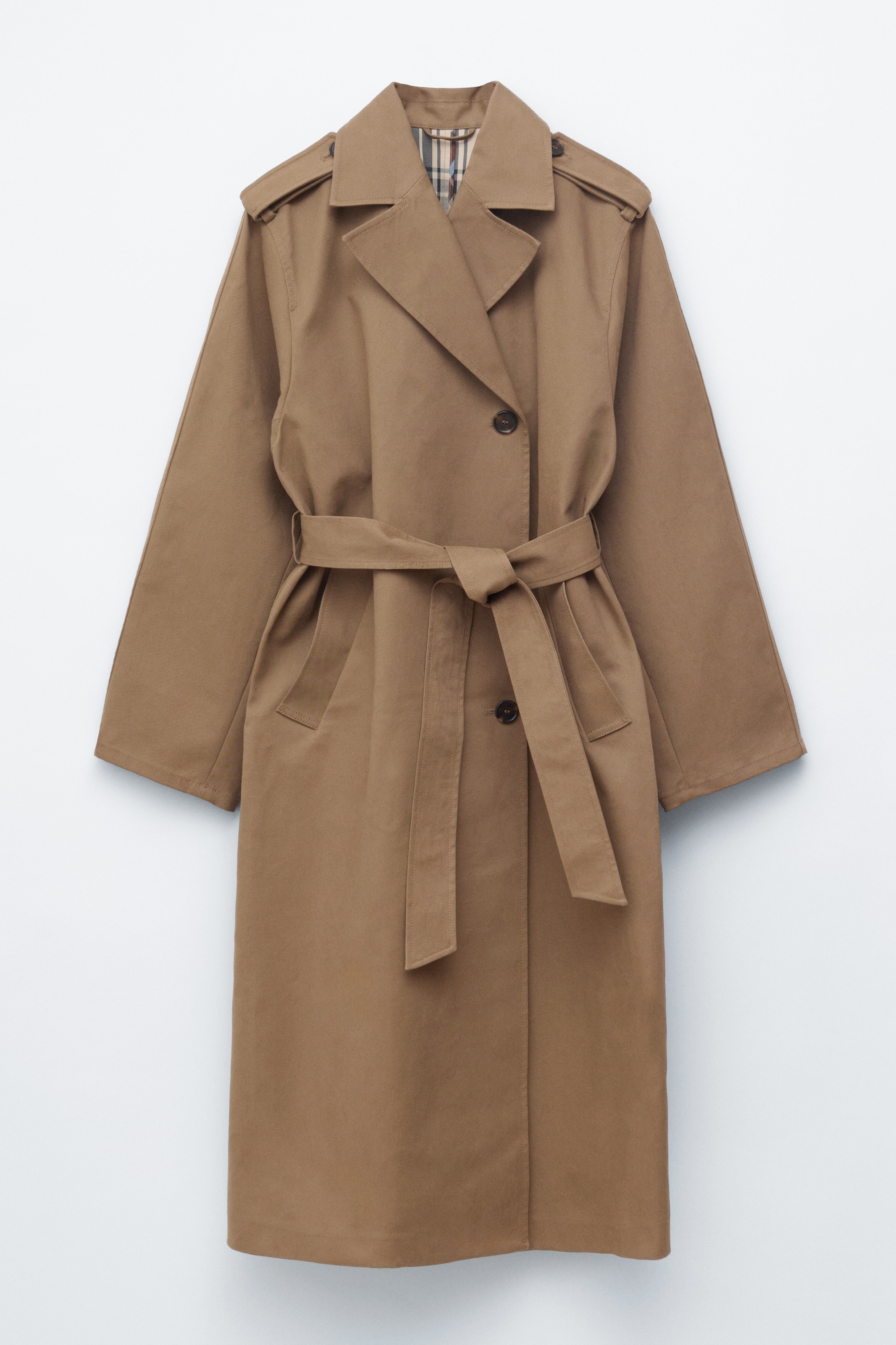 Agrandir l'image: Un trench-coat beige est présenté de face, mettant en avant des revers crantés, des pattes d'épaule et une ceinture en tissu assorti nouée à la taille. Des boutons sombres sont visibles sur la fermeture avant, et une doublure à carreaux apparaît sur le col intérieur.