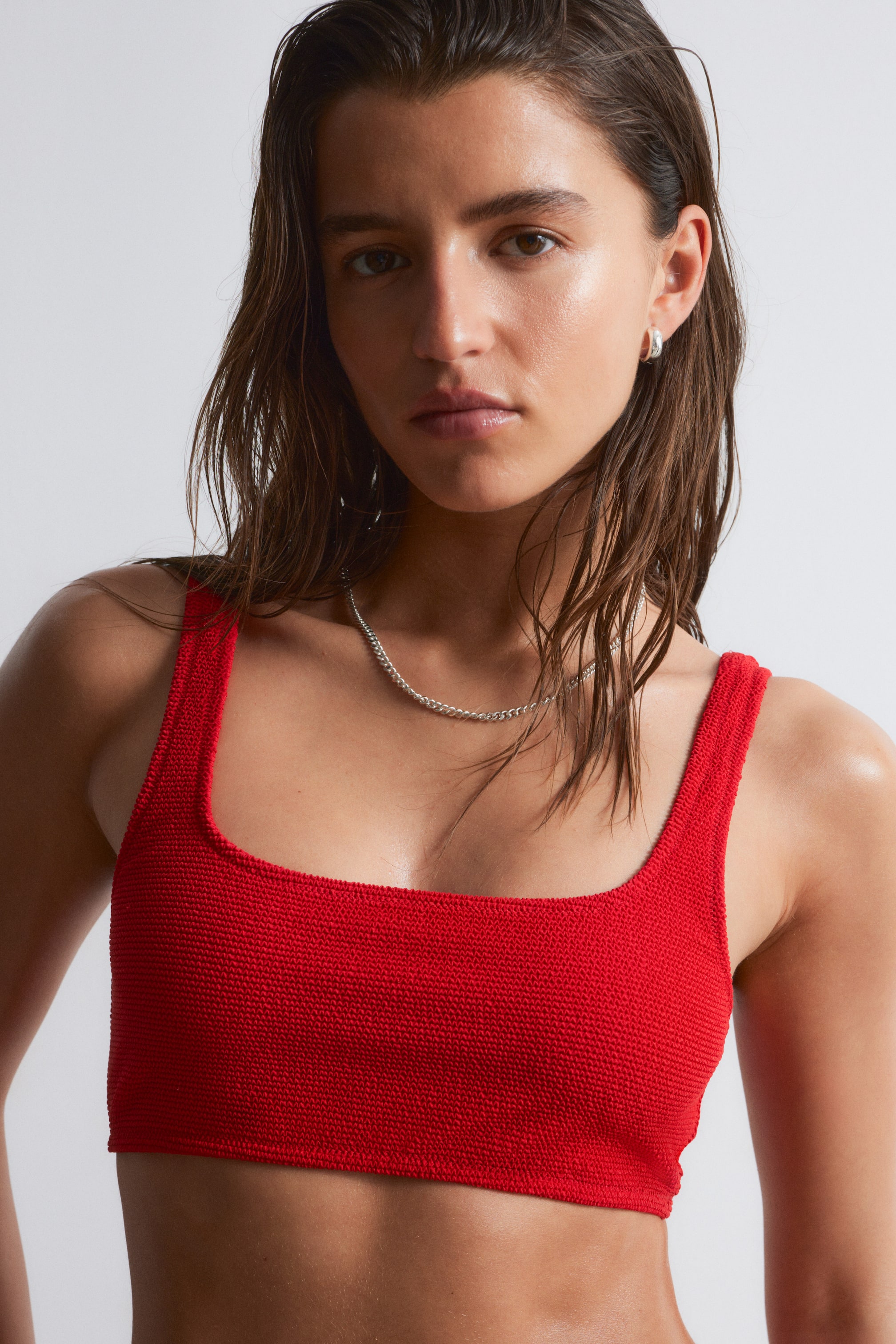 Se større billede: En rød tekstureret bikinioverdel med en lige halsudskæring bæres af modellen. En sølvkædehalskæde hviler på toppen.