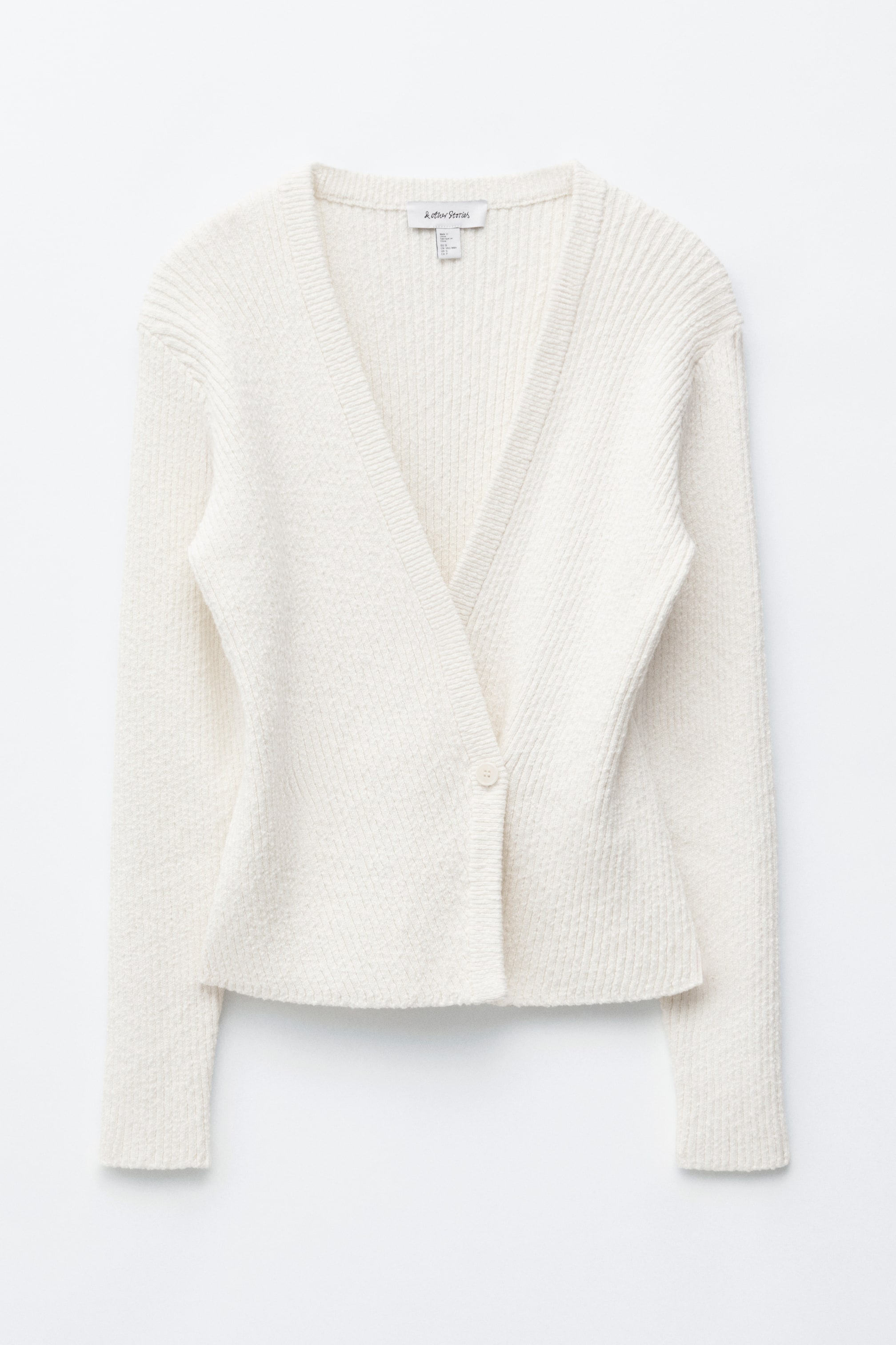 Ver imagem maior: Um cardigan de cor creme apresenta a sua vista frontal, com um design de decote em V cruzado. Exibe um fecho de botão único no lado esquerdo da parte frontal, com detalhes em malha canelada nos ombros e mangas superiores, e uma malha texturizada e ligeiramente felpuda no corpo principal e mangas inferiores.