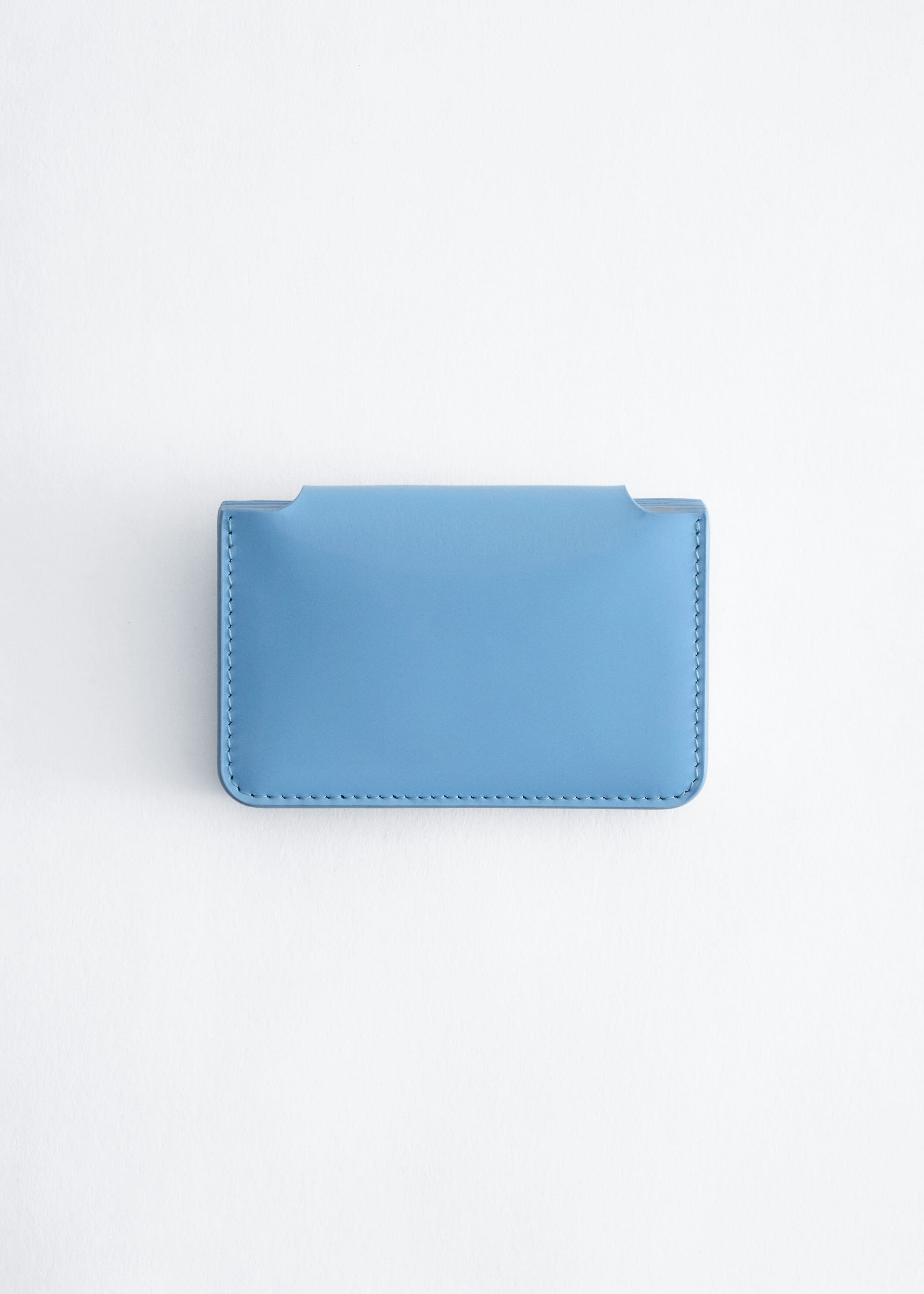 A light blue leather cardholder is shown from the back, featuring a smooth rectangular shape, tone-on-tone perimeter stitching, and a folded top flap.