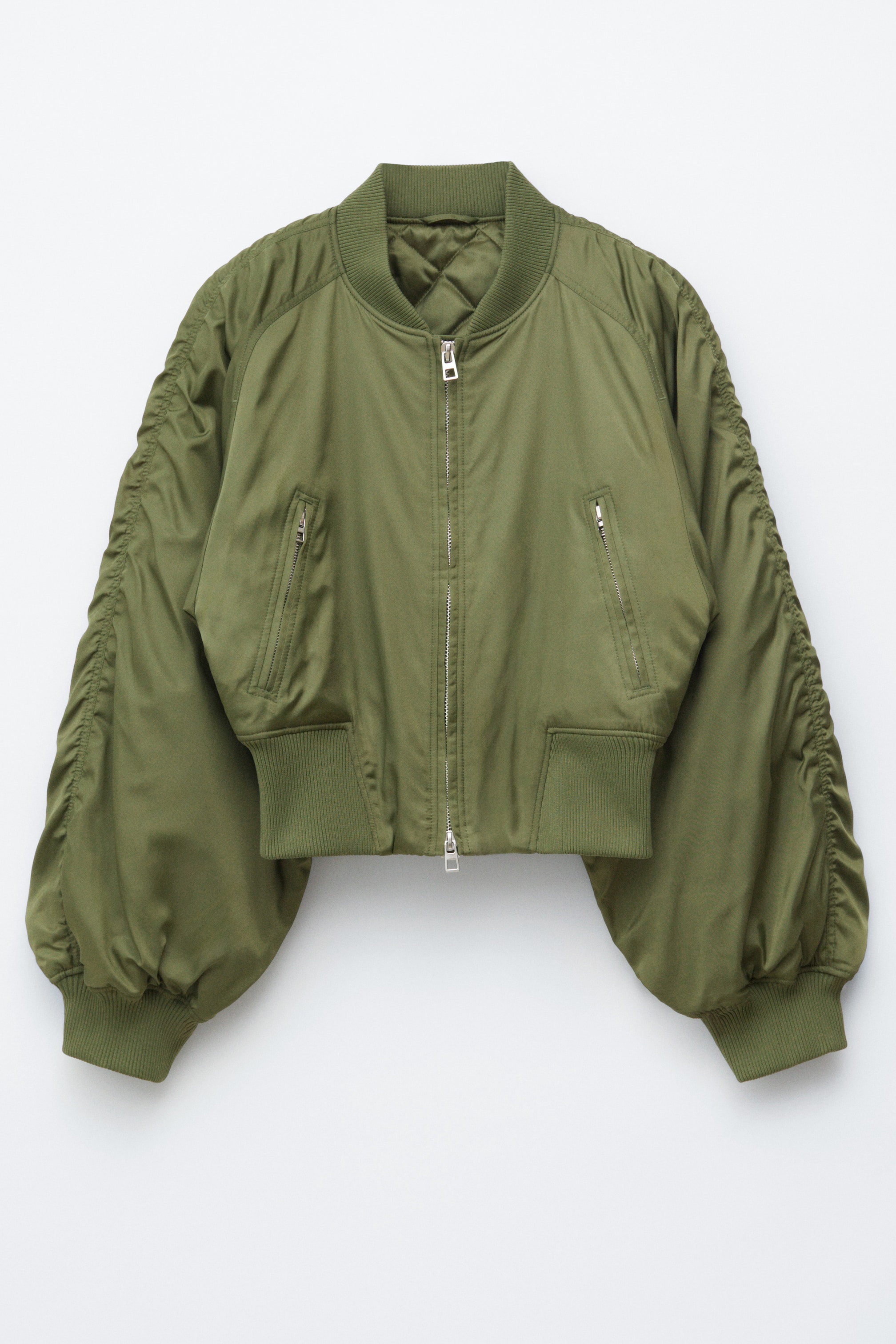 View larger image: An olive green bomber jacket is displayed in its front view, showcasing a cropped, boxy silhouette with voluminous sleeves that exhibit puckered seams. It also features a ribbed collar, cuffs, and hem, two jetted zip pockets, a two-way front zip fastening, and a quilted lining visible at the collar.