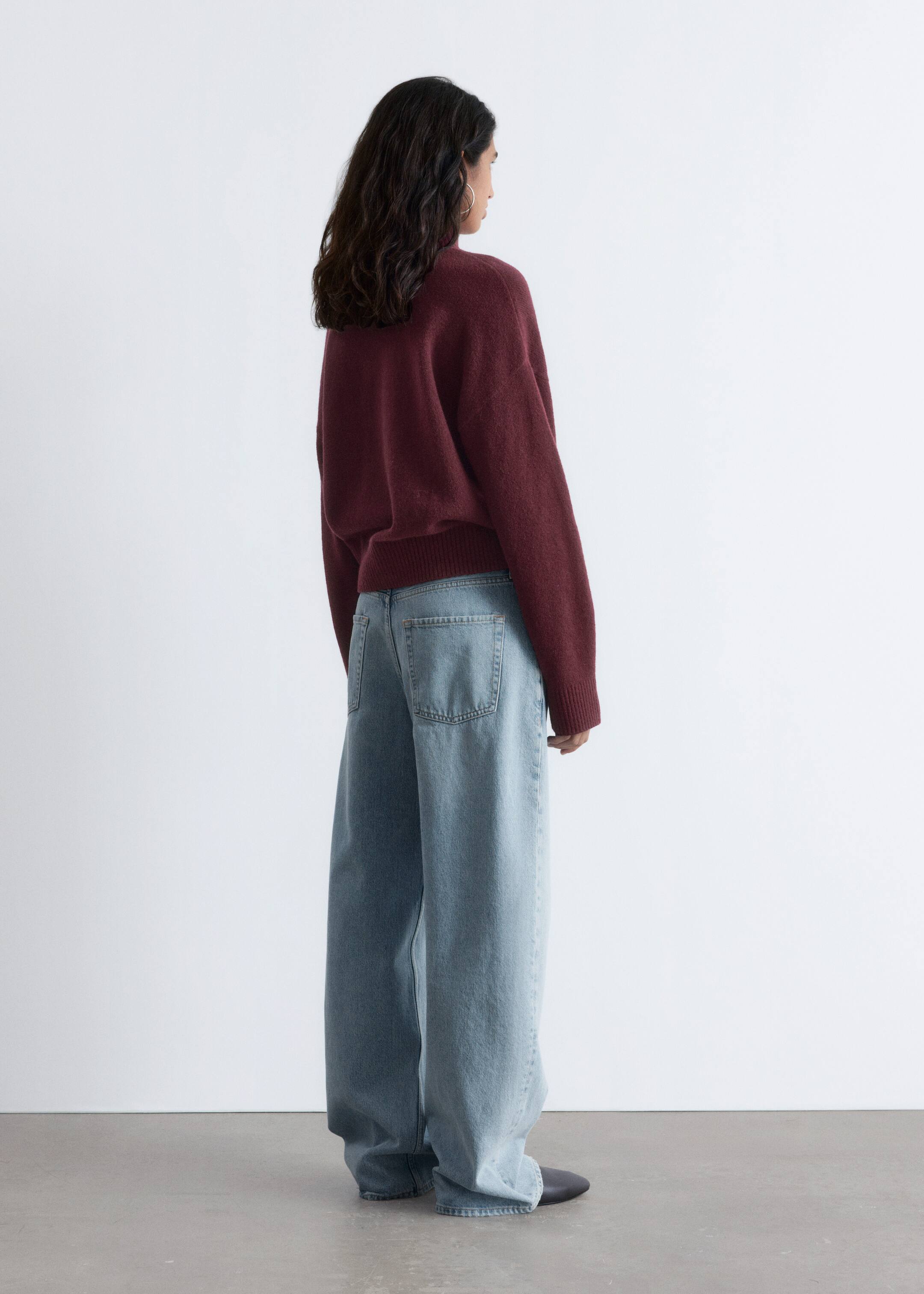 View larger image: A dark red, relaxed-fit sweater is being presented from the back view, its ribbed hem and cuffs appearing slightly bloused over light wash, wide-leg jeans. The jeans are showcasing a loose silhouette with visible back pockets.