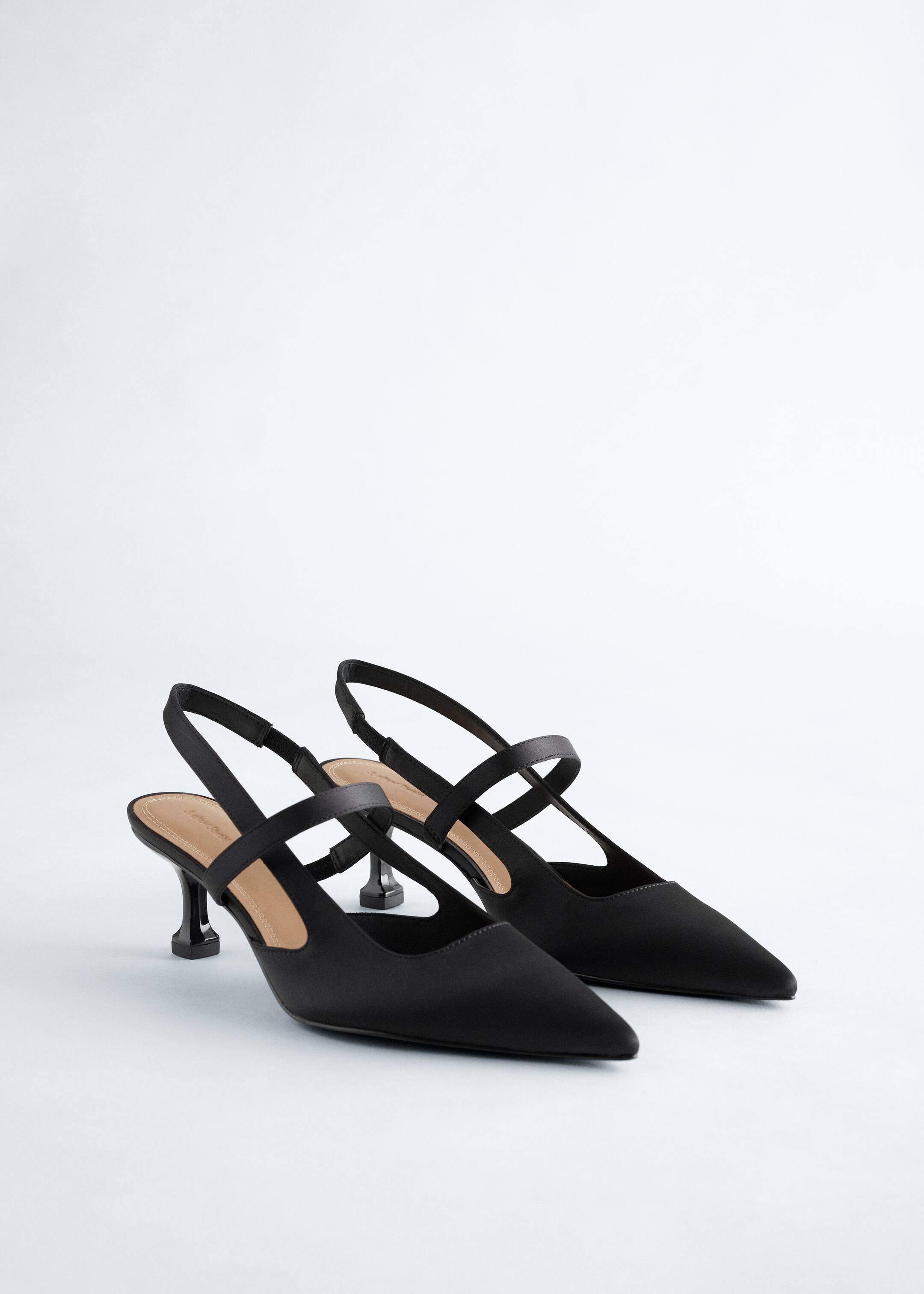 Nagyobb kép megtekintése: Egy pár fekete slingback cipő balra dőlve van bemutatva, hegyes orral és szoborszerű kis sarkakkal. Mindegyik cipő egy slingback pánttal és egy további pánttal a lábfej felett van tervezve, világosbarna talpbetétet mutatva.