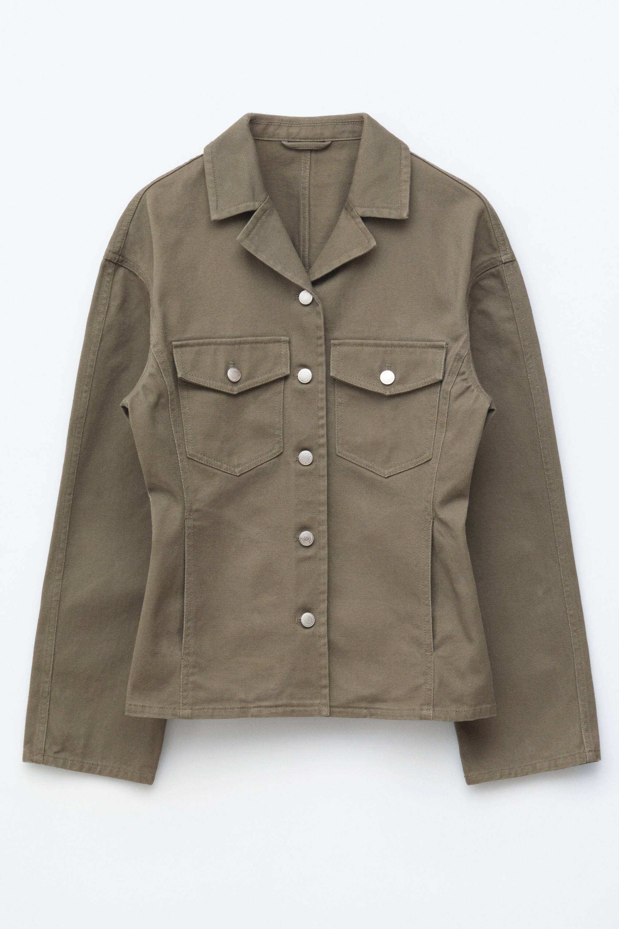 Ver imagem maior: A jaqueta caqui é apresentada de frente, com uma gola pontiaguda e uma coluna central de botões de pressão prateados. Exibe dois bolsos com aba no peito com botões de pressão prateados, uma cintura ajustada definida por costuras pespontadas e bolsos embutidos nas laterais.