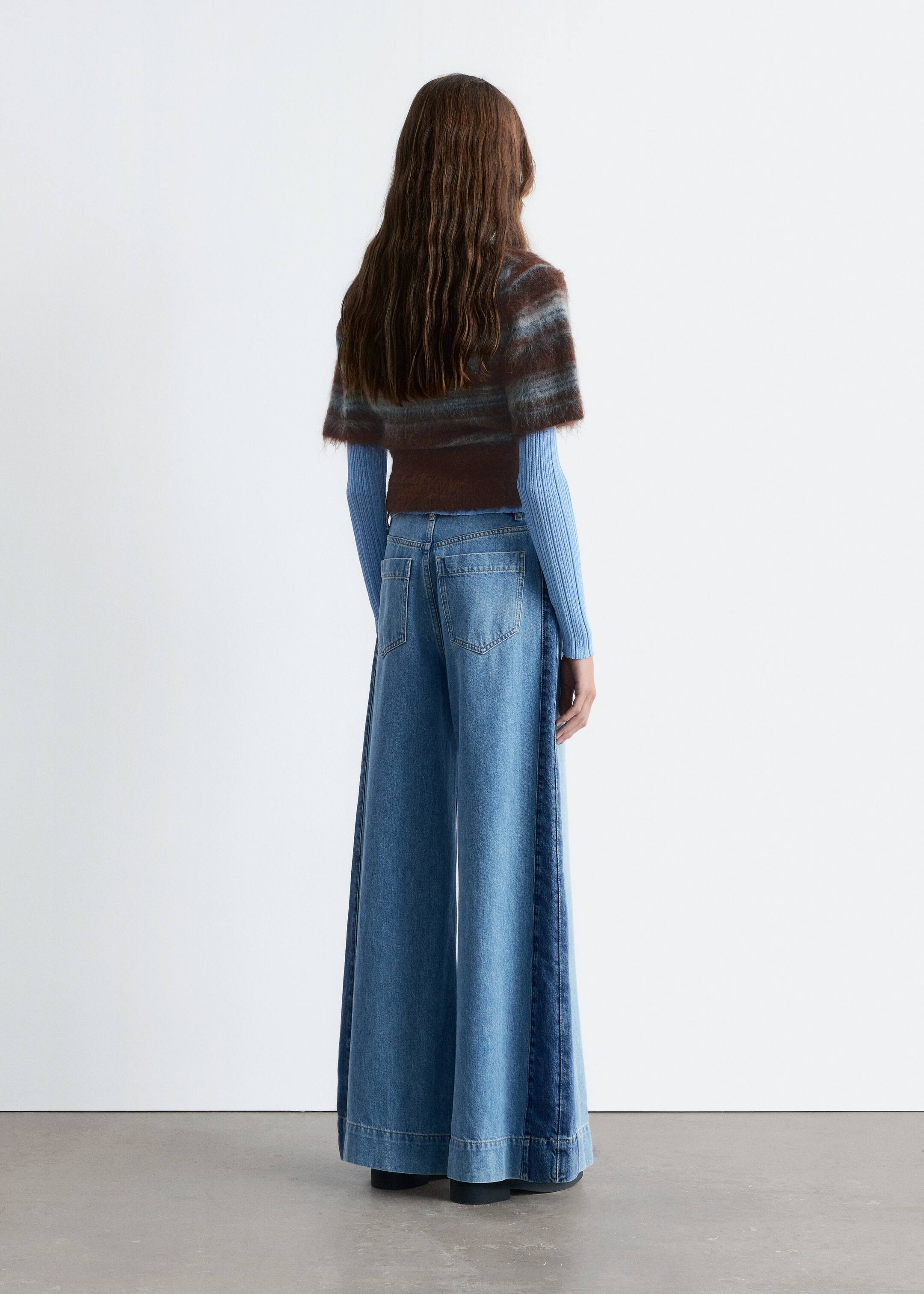 Agrandir l'image: Le mannequin porte un jean taille haute, mettant en valeur une silhouette large et longue avec des détails de panneaux latéraux le long des jambes et un ourlet large surpiqué.