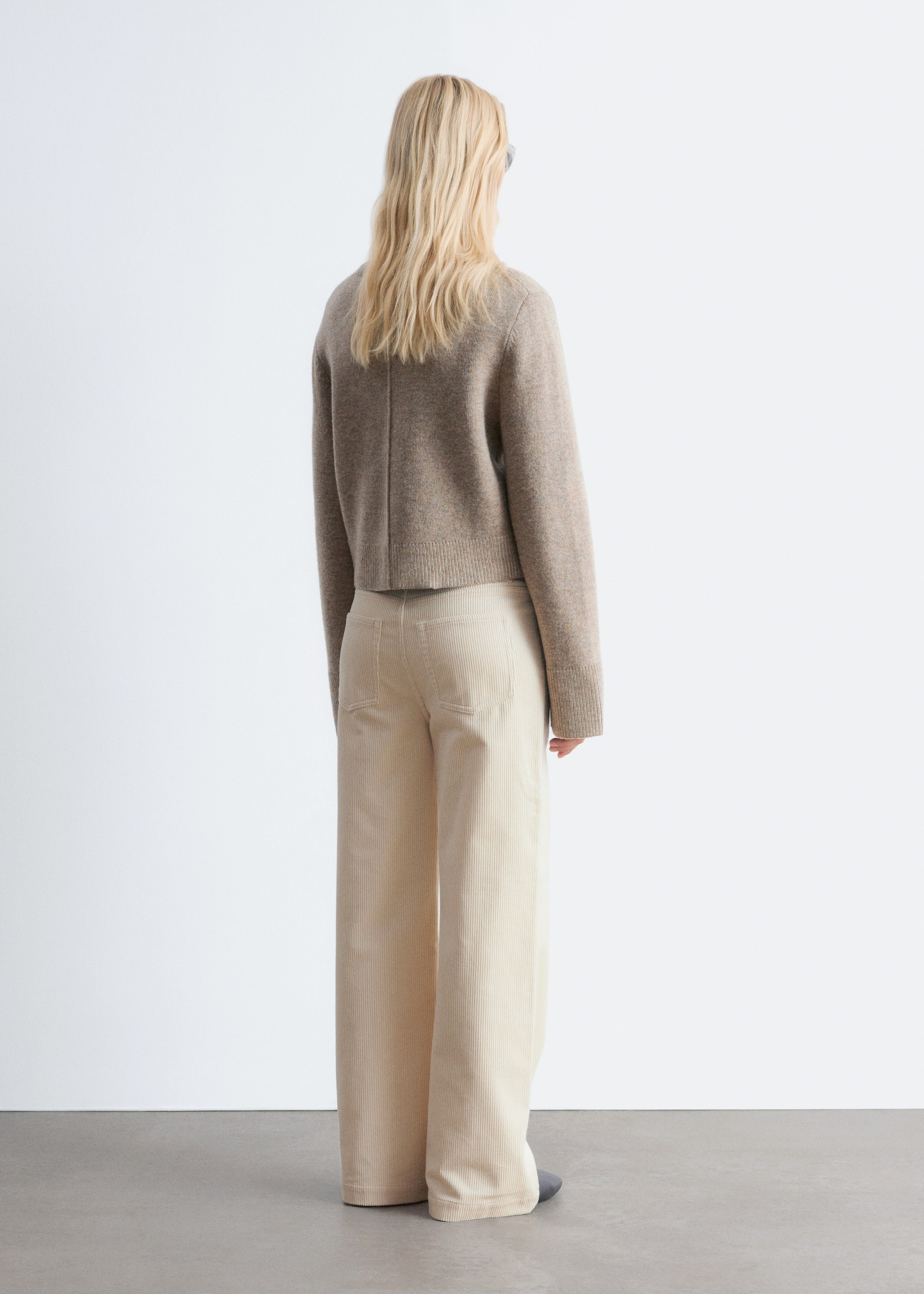Ver imagen más grande: Un suéter de punto beige jaspeado se muestra desde atrás, con un largo recortado, un dobladillo ancho acanalado y una costura vertical que corre por el centro. Se combina con pantalones de pana de pierna ancha en color crema claro, que presentan canales verticales visibles y dos bolsillos traseros de parche.
