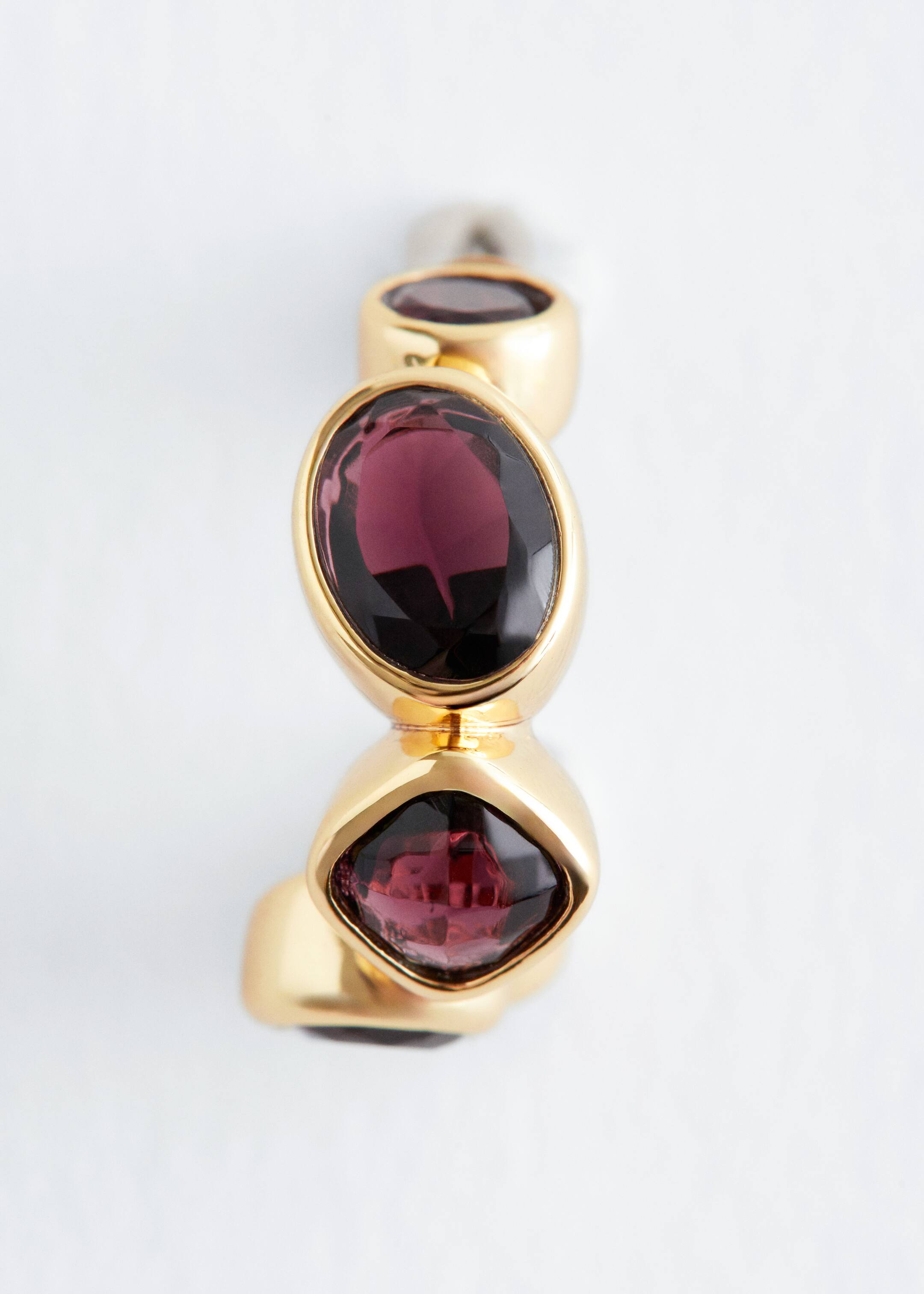 Agrandir l'image: Une boucle d'oreille en forme de créole de couleur or est vue de dessus, affichant trois cristaux facettés de couleur violet foncé. Deux des cristaux sont de forme ovale, et un est un carré arrondi, tous incrustés le long de la courbe de la boucle d'oreille.