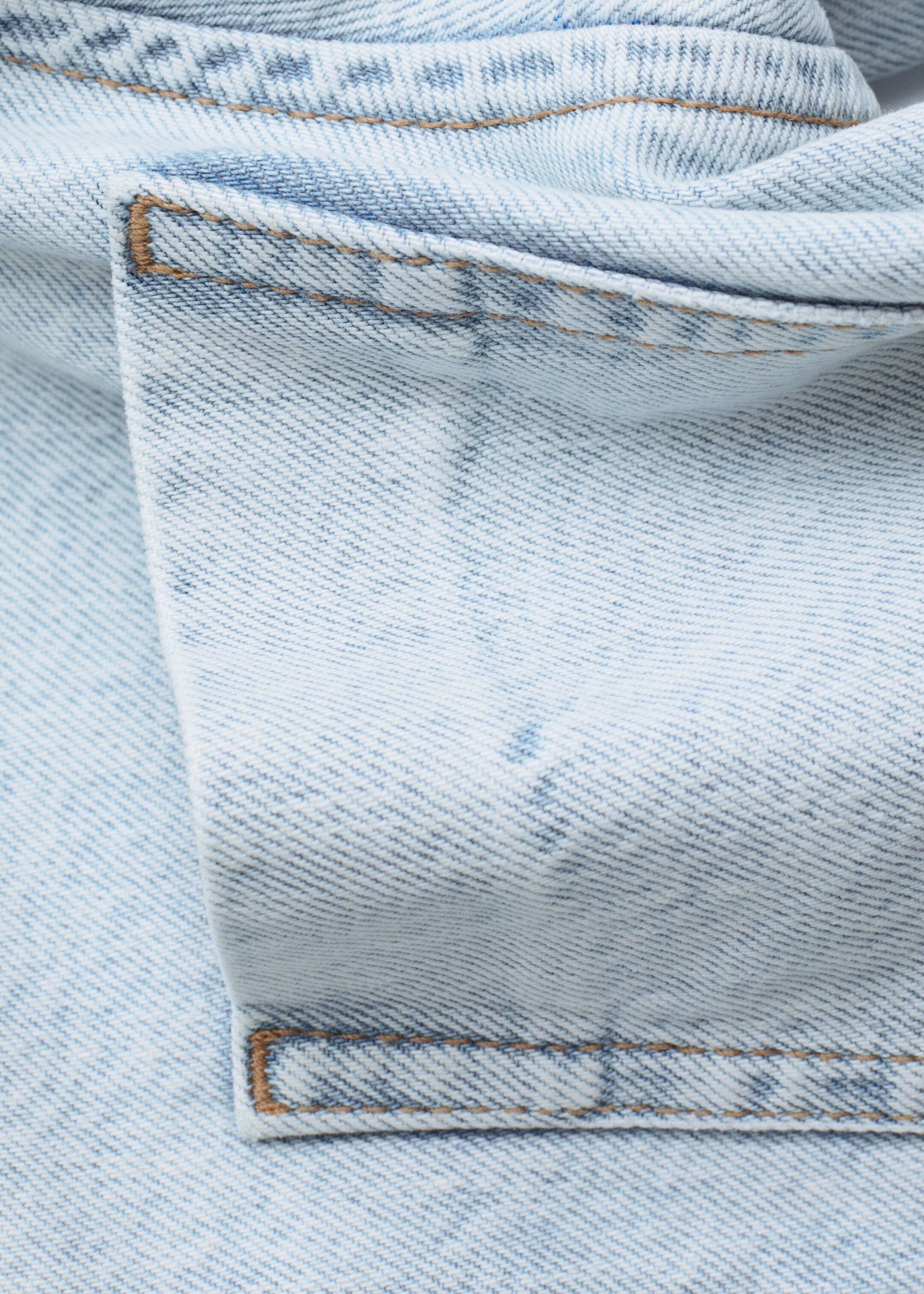 View larger image: Light-wash denim fabric is featuring a faded blue color with a visible diagonal twill weave texture. Contrasting brownish-orange stitching is forming bar tack reinforcements and double seams on the folded material.