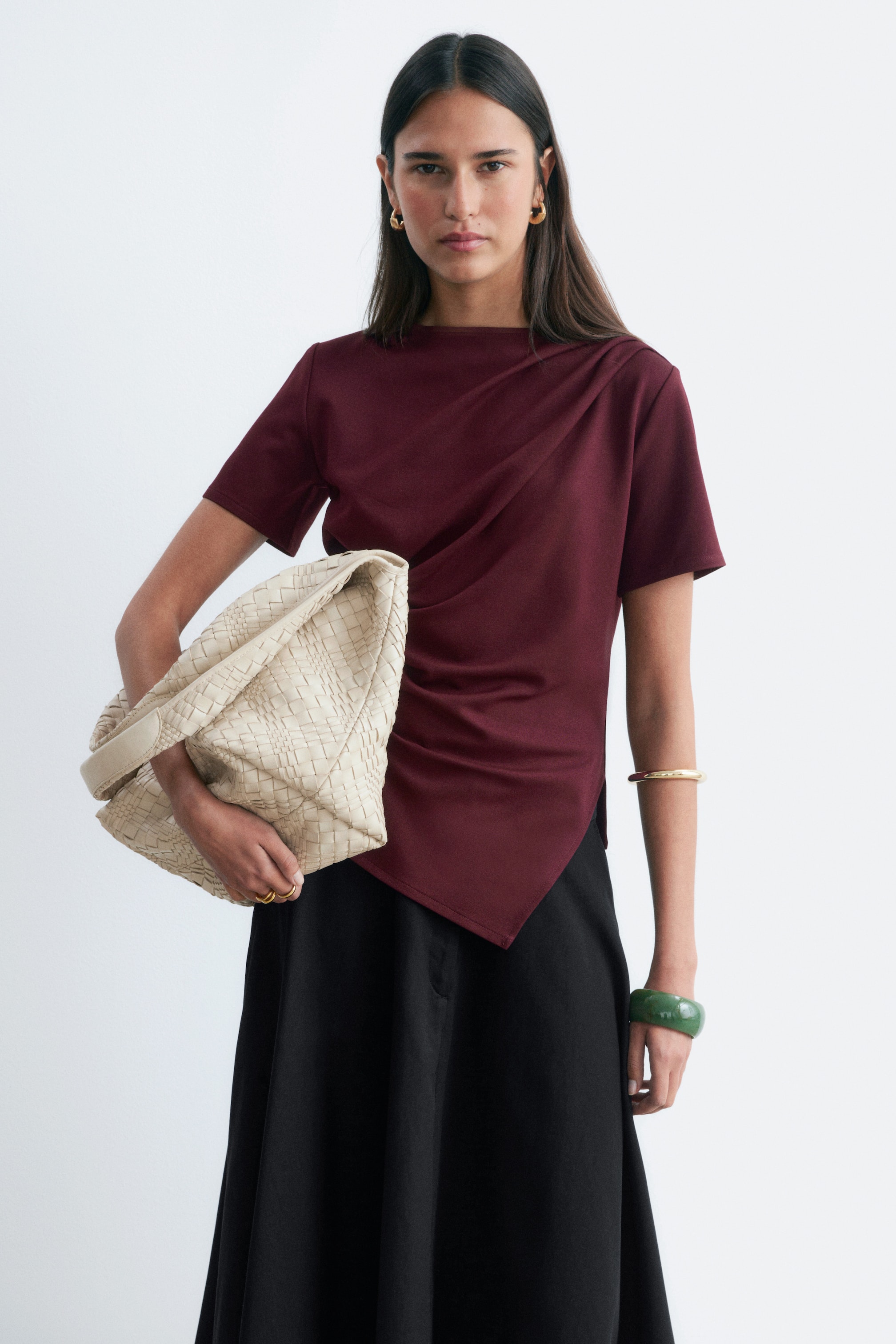 Visa större bild: En vinröd topp med korta ärmar, bred ringning och en asymmetrisk draperad framdel med sned nederkant, som bärs tillsammans med en svart, följsam midikjol.