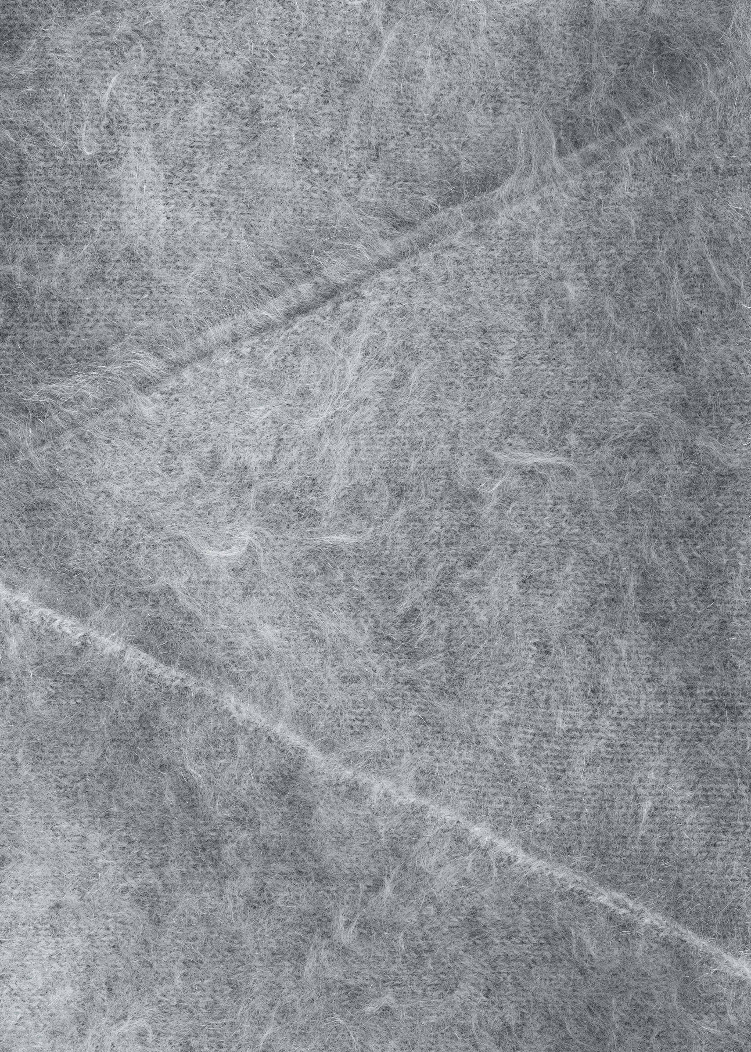 A close-up of a light gray brushed knit fabric featuring a fuzzy, shaggy texture with long, fine fibers. Two diagonal stitched seams run across the surface, highlighting the construction of the soft material.