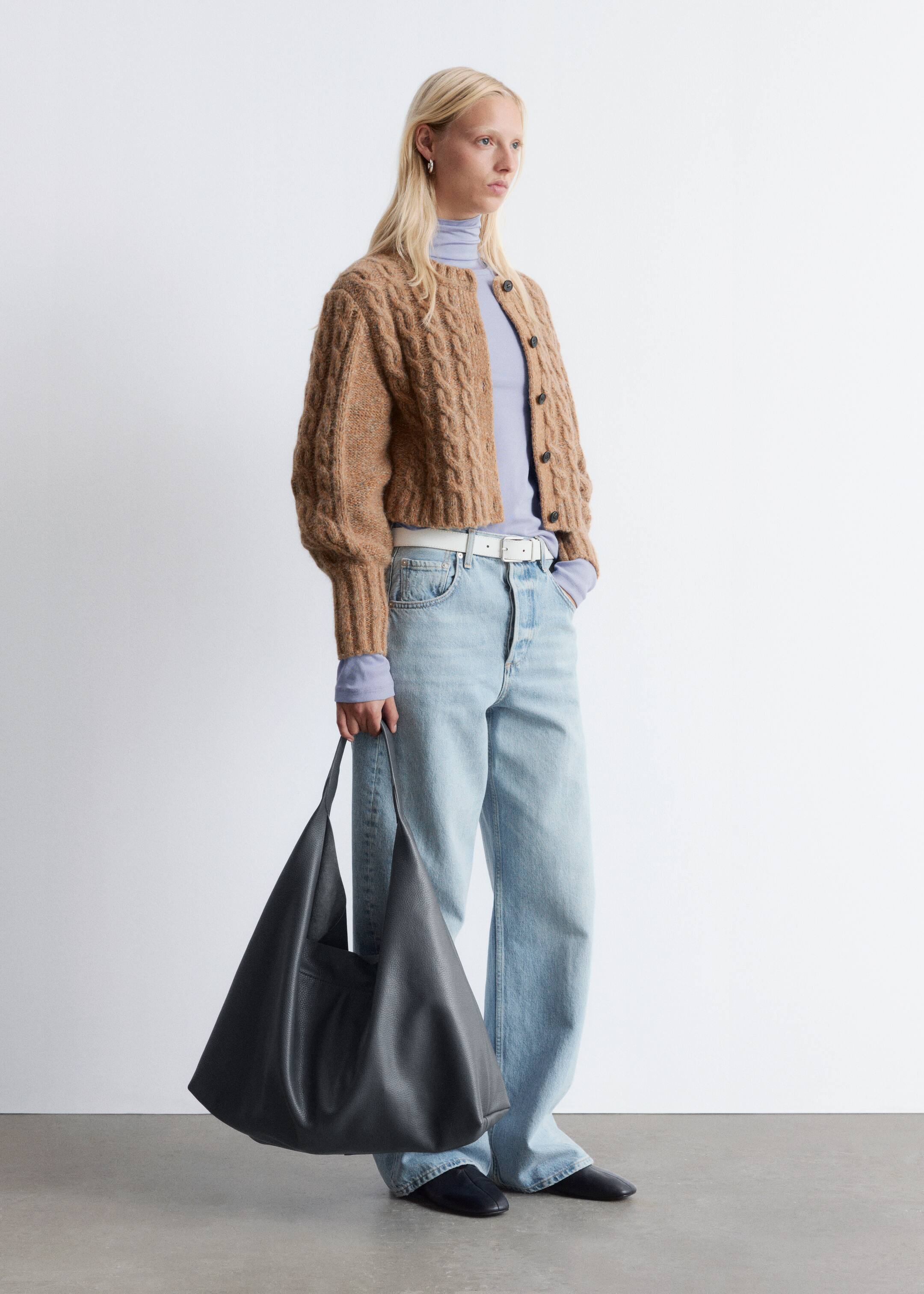 Agrandir l'image: Un cardigan en maille torsadée brun est porté par le modèle, présentant une silhouette raccourcie, un col rond, des manches bouffantes volumineuses et des finitions côtelées. Des boutons foncés ferment le devant, et il est superposé sur un haut violet clair.
