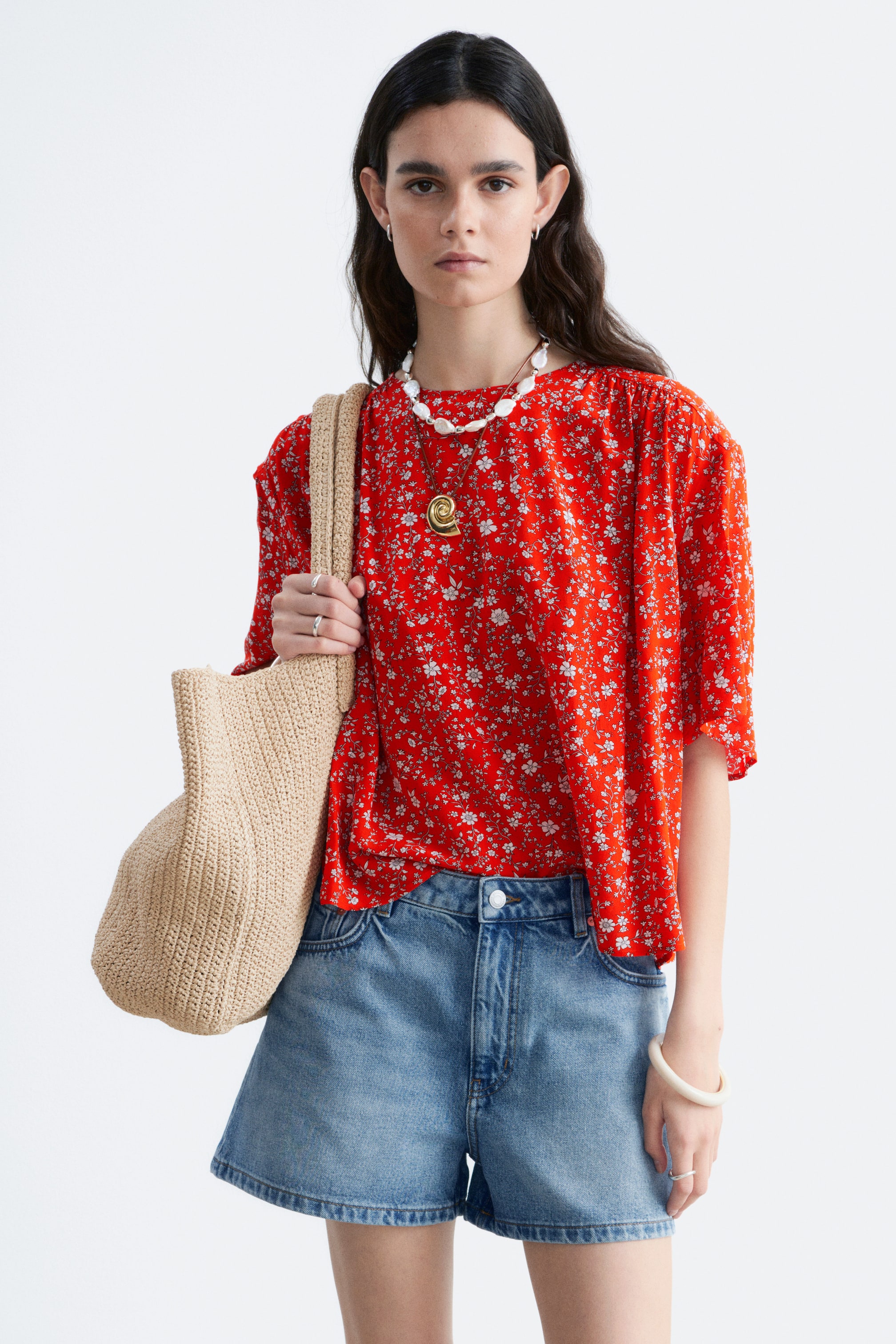 Ver imagen más grande: Top floral rojo con cuello redondo y mangas cortas abullonadas. Presenta un corte holgado, con el dobladillo parcialmente metido en unos shorts de mezclilla azul.