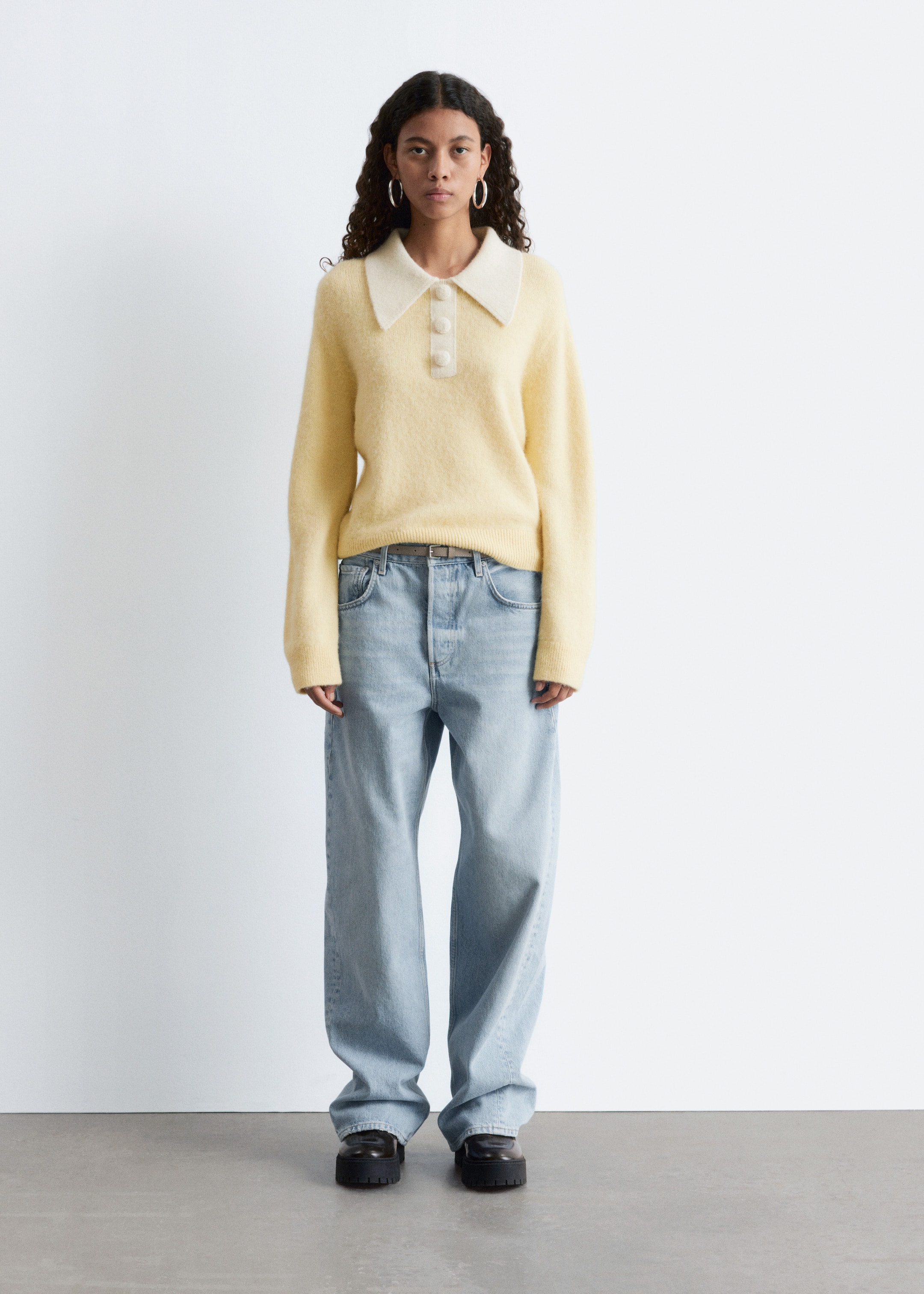 View larger image: A light yellow knitted jumper, featuring an oversized cream collar and a three-button placket with covered buttons, is being worn by the model. The jumper is displaying long sleeves with ribbed cuffs and a ribbed hem, and is being styled over light-wash jeans.
