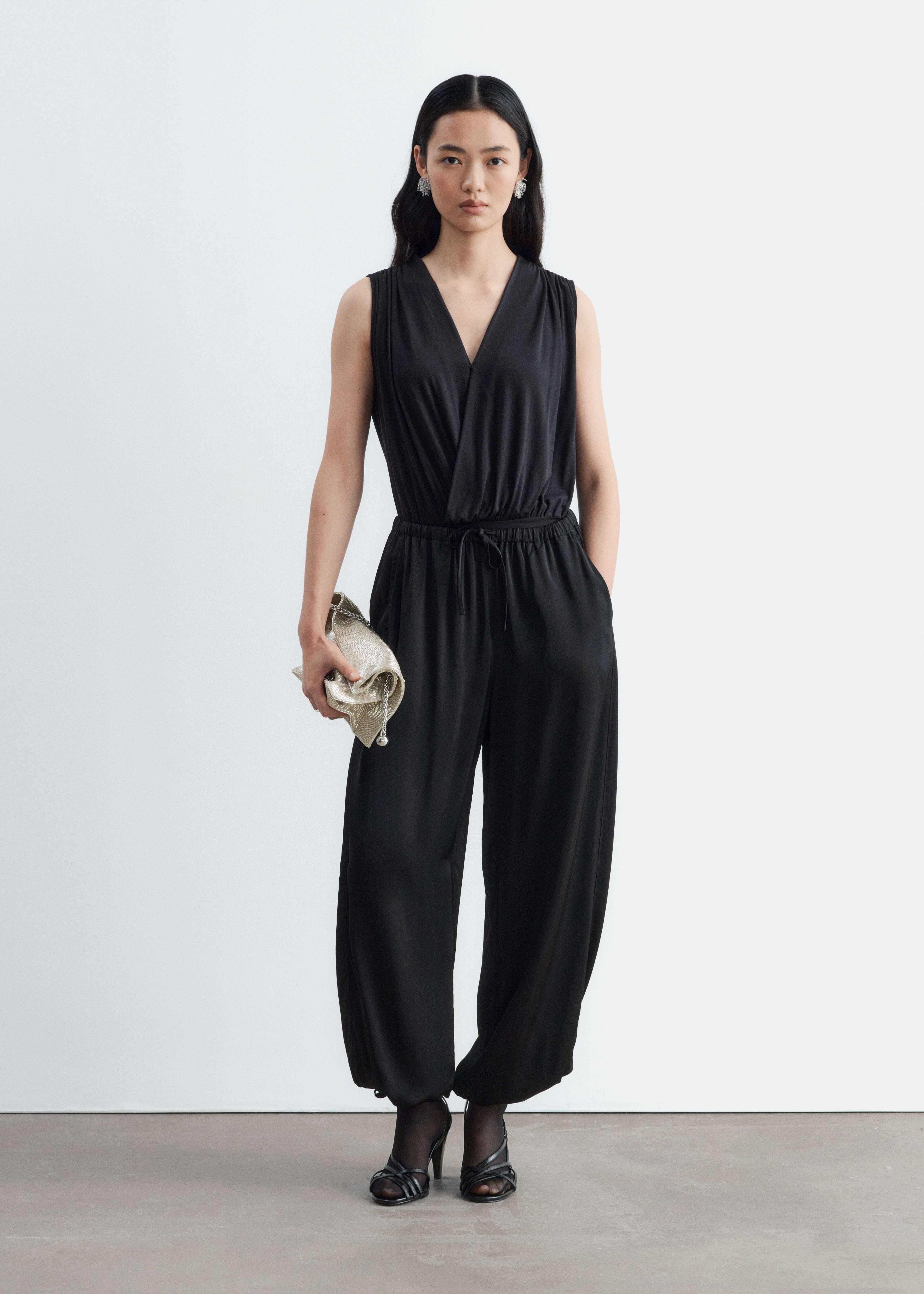 Los pantalones balloon negros se muestran de frente, con una silueta holgada y voluminosa confeccionada en un tejido negro fluido con un sutil brillo. EstÃ¡n diseÃ±ados con una cintura elÃ¡stica con cordÃ³n ajustable y bajos fruncidos con finos lazos colgantes.