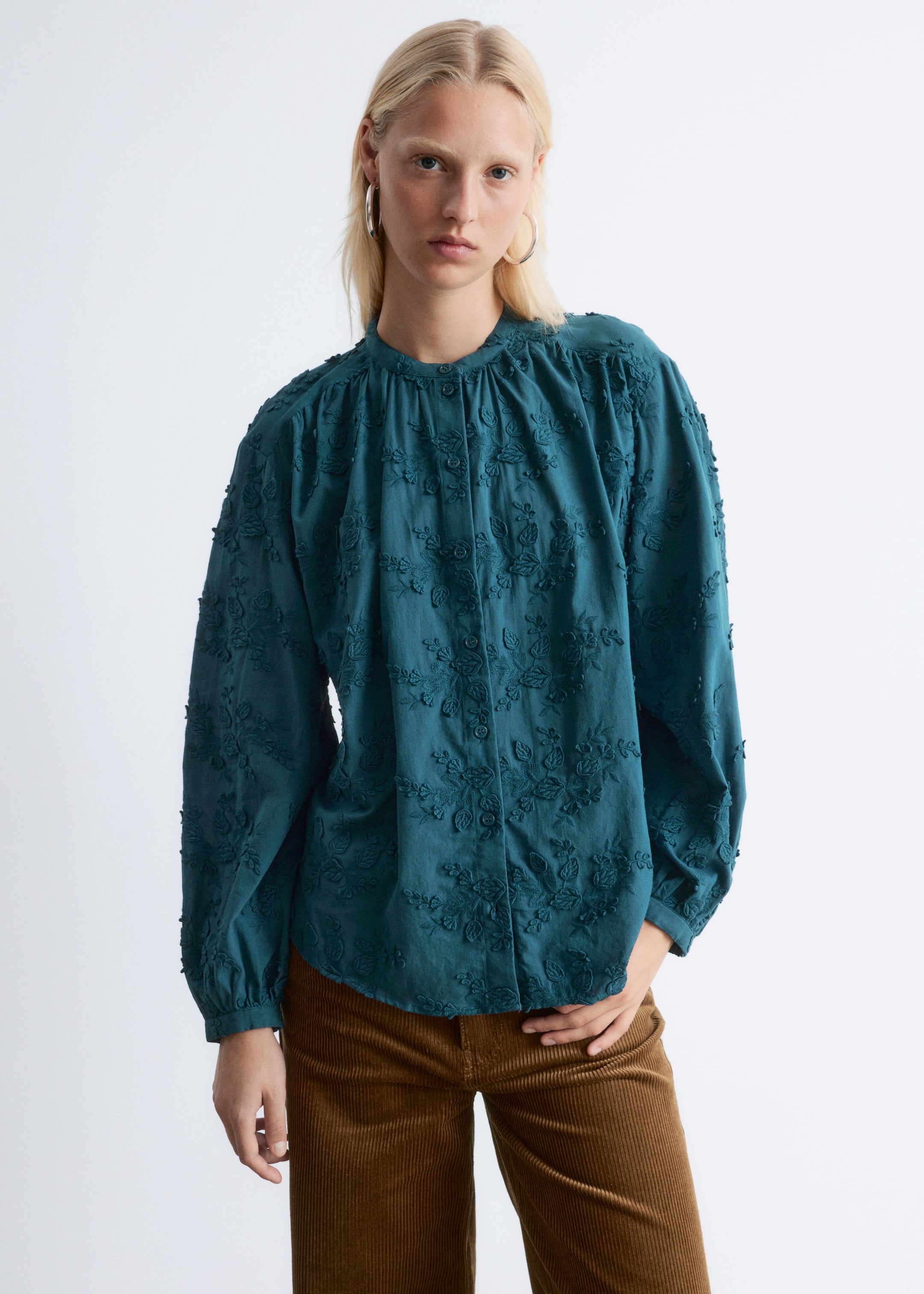Visualizza immagine più grande: Una blusa color verde acqua a maniche lunghe, presentata di fronte, è caratterizzata da un colletto alla coreana, una chiusura frontale completa di bottoni, ricami floreali in rilievo su tutta la superficie, spalle arricciate e polsini elasticizzati.
