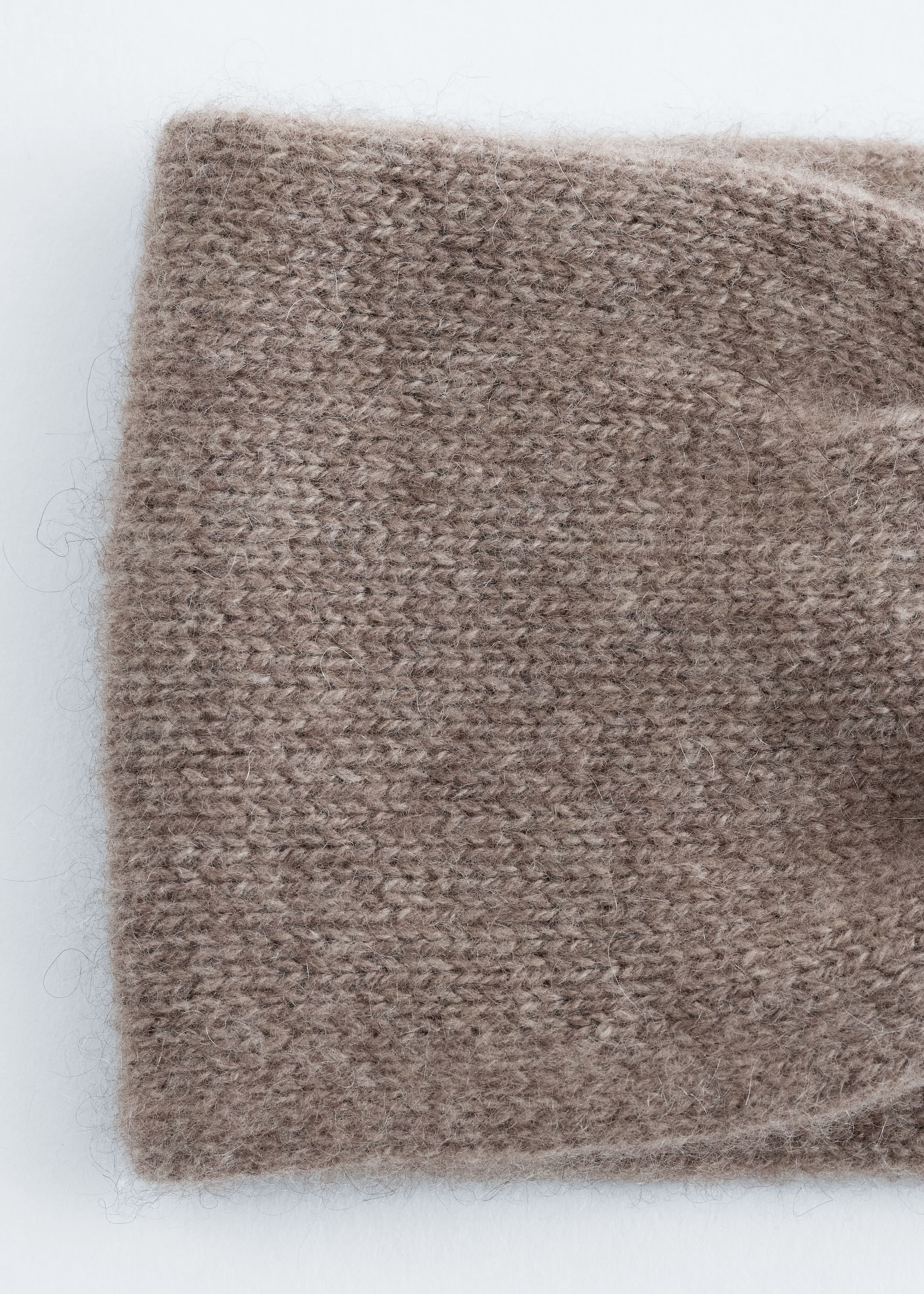 Grösseres Bild ansehen: Ein breites, taupefarbenes Strickstirnband aus Kaschmir zeichnet sich durch eine weiche Textur und einen sichtbaren zentralen Drehknoten auf der rechten Seite aus.