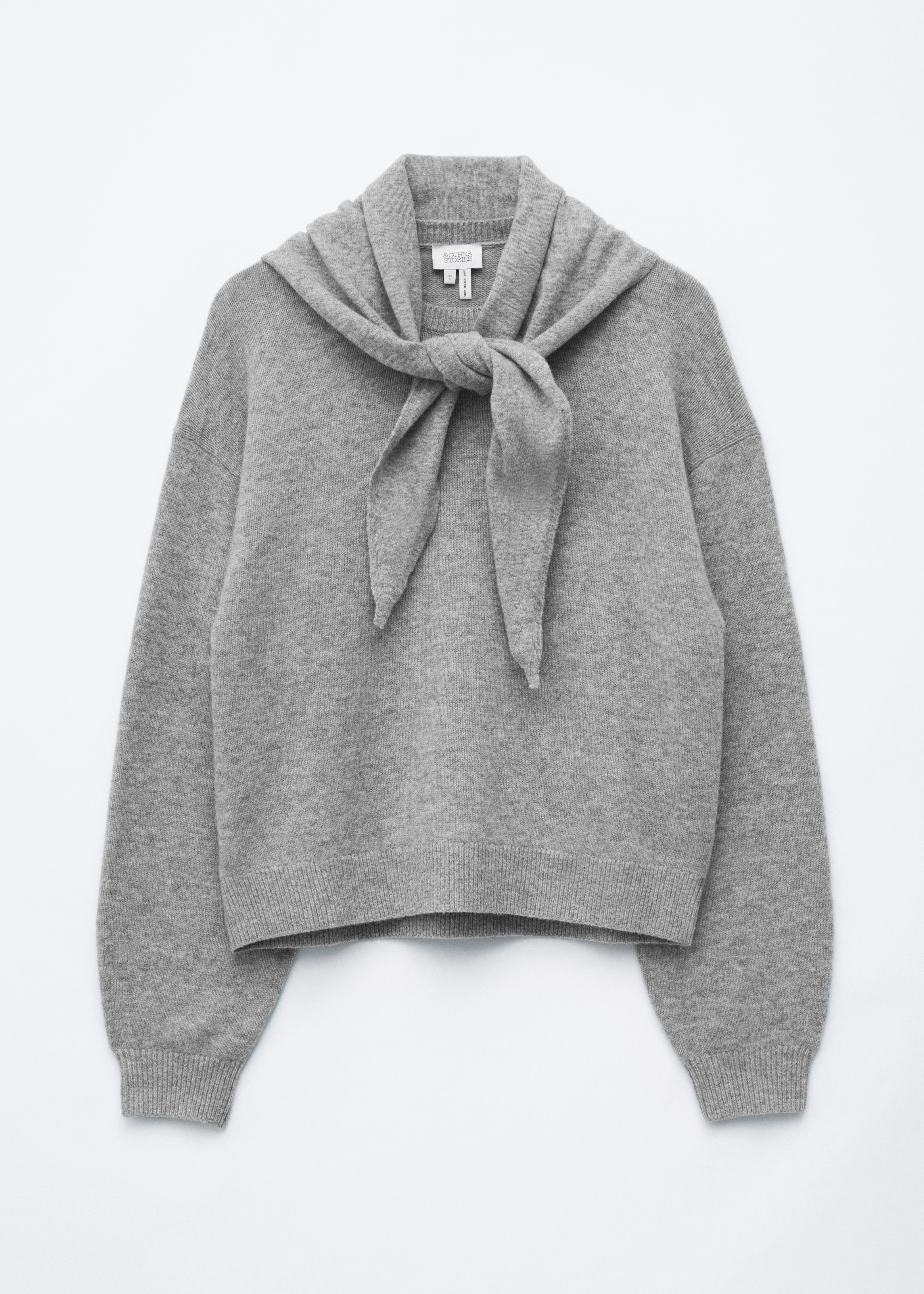 Un maglione in lana merino grigio mÃ©lange, dalla vestibilitÃ  rilassata, con polsini a coste e un dettaglio sciarpa integrato annodato morbidamente al collo, indossato dalla modella. Il maglione Ã¨ abbinato infilato in una gonna scozzese grigio scuro, mentre la modella tiene in mano una pochette in pelle nera arricciata.