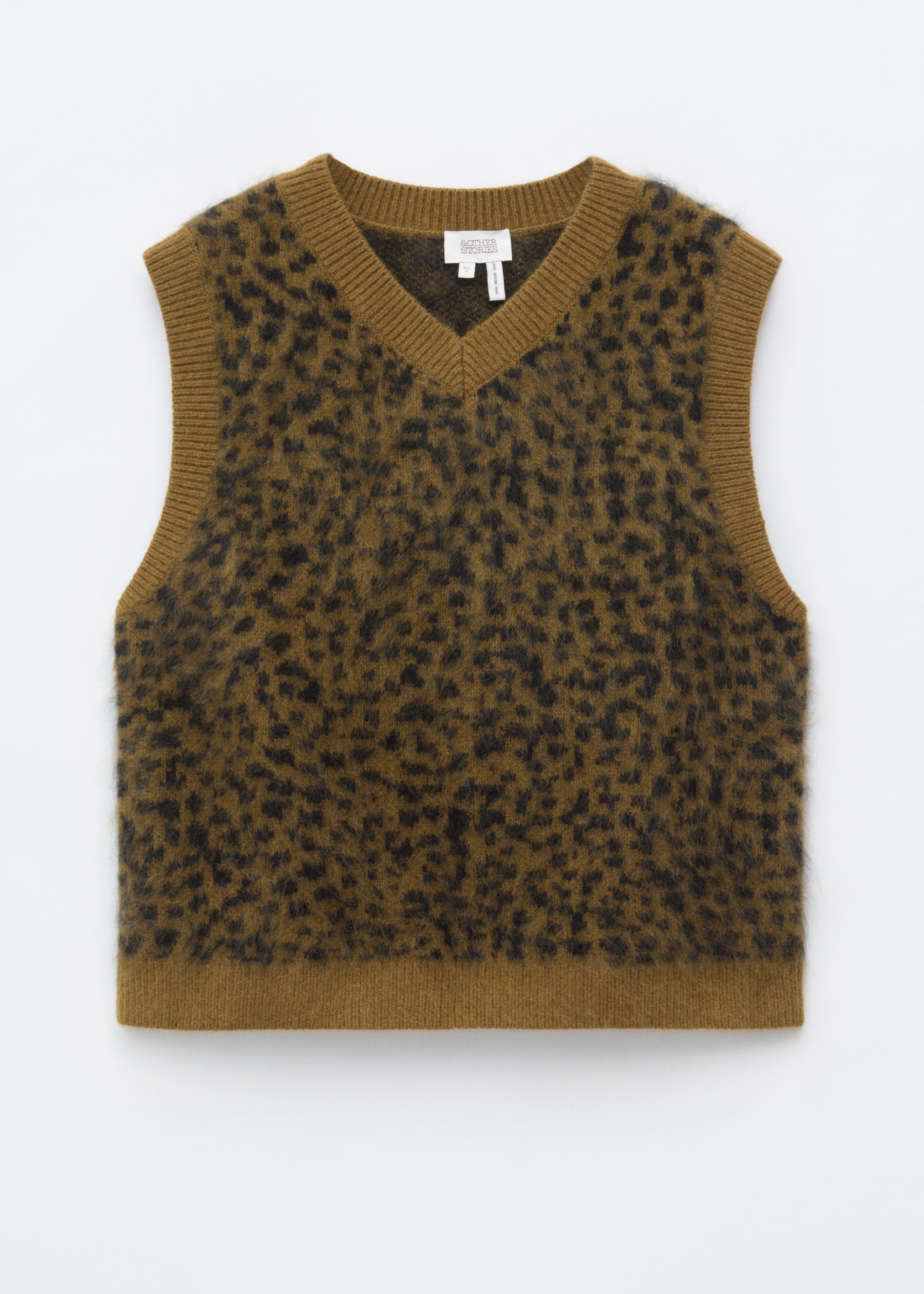Un pulover fÄrÄ mÃ¢neci din lÃ¢nÄ, cu un corp jacard pufos, cu imprimeu leopard, Èi borduri striate verde-oliv este purtat de model. Puloverul fÄrÄ mÃ¢neci cu decolteu Ã®n V este purtat peste o cÄmaÈÄ bleu cu nasturi Èi stilizat cu o fustÄ Ã®nchisÄ la culoare, plisatÄ.