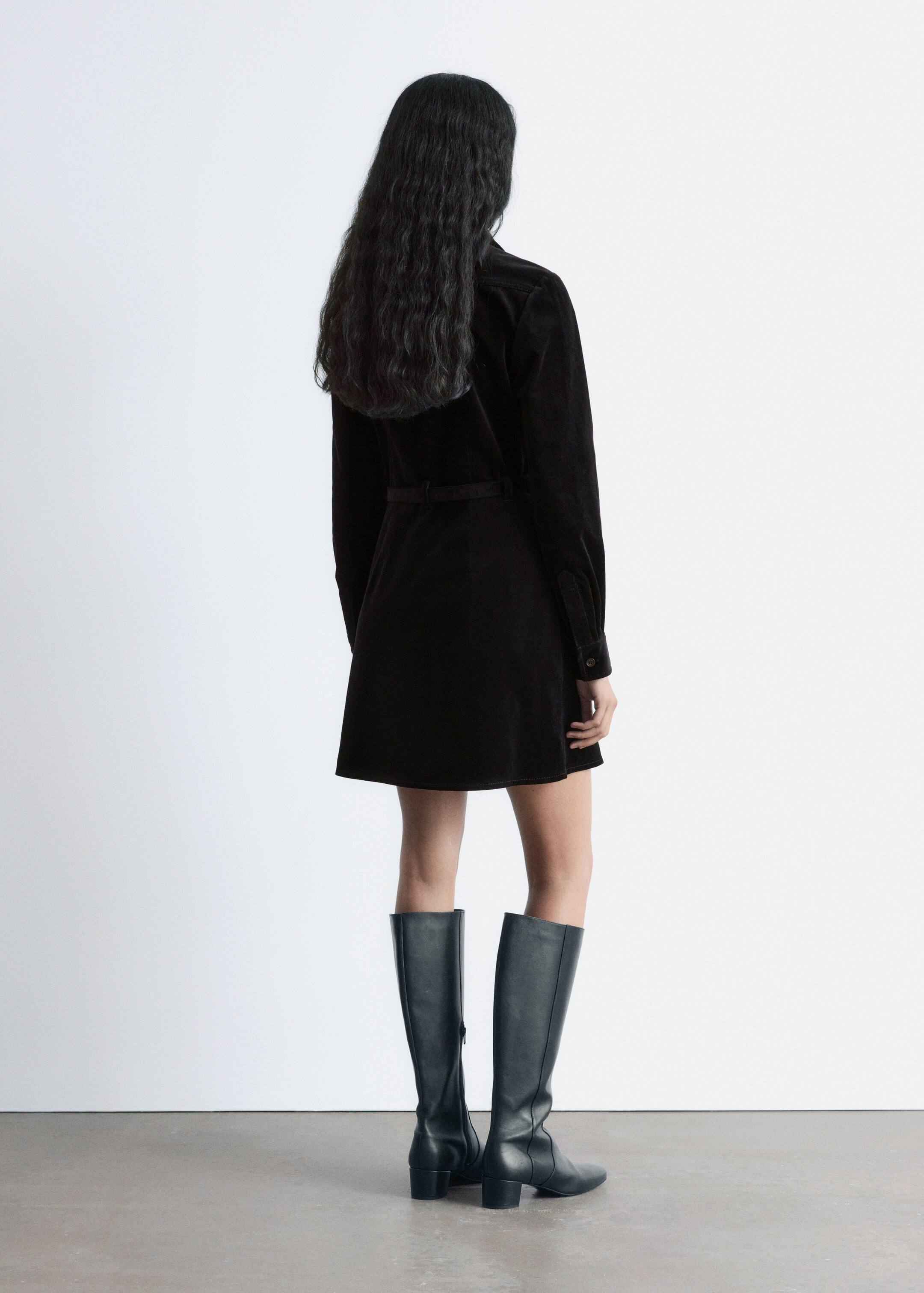 Agrandir l'image: Une robe mini en velours côtelé noir est présentée de dos. Elle présente une silhouette de style chemise avec un col visible, des manches longues avec des poignets boutonnés, et une ceinture assortie cintrant la taille.