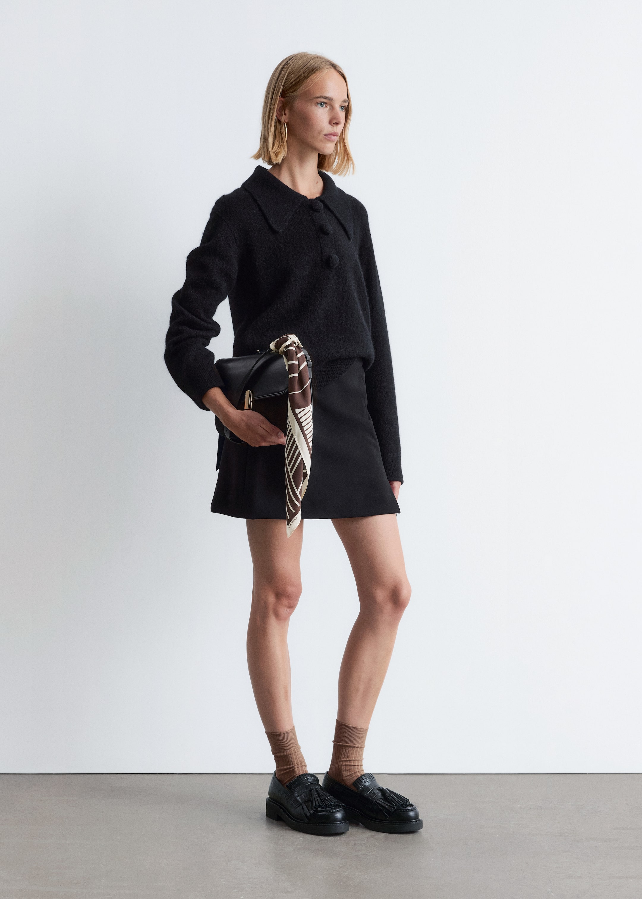 Agrandir l'image: Un pull noir en tricot duveteux est porté, vu sous un léger angle latéral. Le pull présente un col pointu et trois grands boutons ronds sur le devant, et est conçu avec des manches longues et une coupe décontractée.