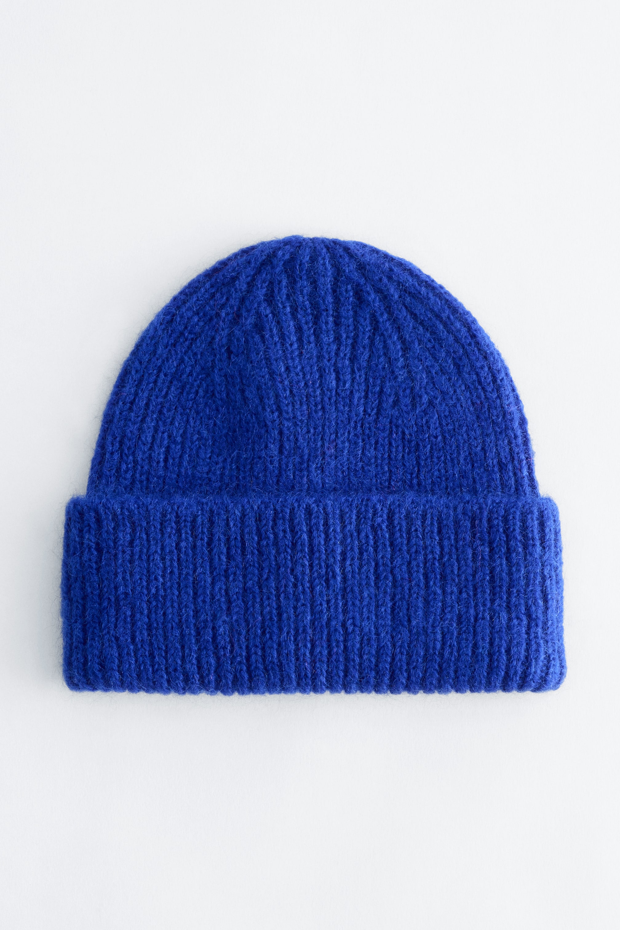 View larger image: A bright blue rib-knit beanie is facing front, showing a visibly fuzzy texture and a wide folded brim.