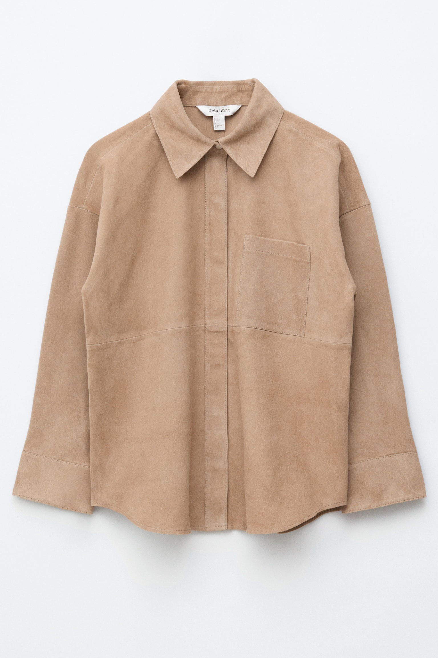 Una camisa de ante color tostado se presenta de FRENTE, con un cuello en punta y una tapeta de longitud completa. Muestra un único bolsillo de parche en el pecho izquierdo, detalles de costura prominentes y mangas largas con aberturas amplias, terminando con un dobladillo curvado.