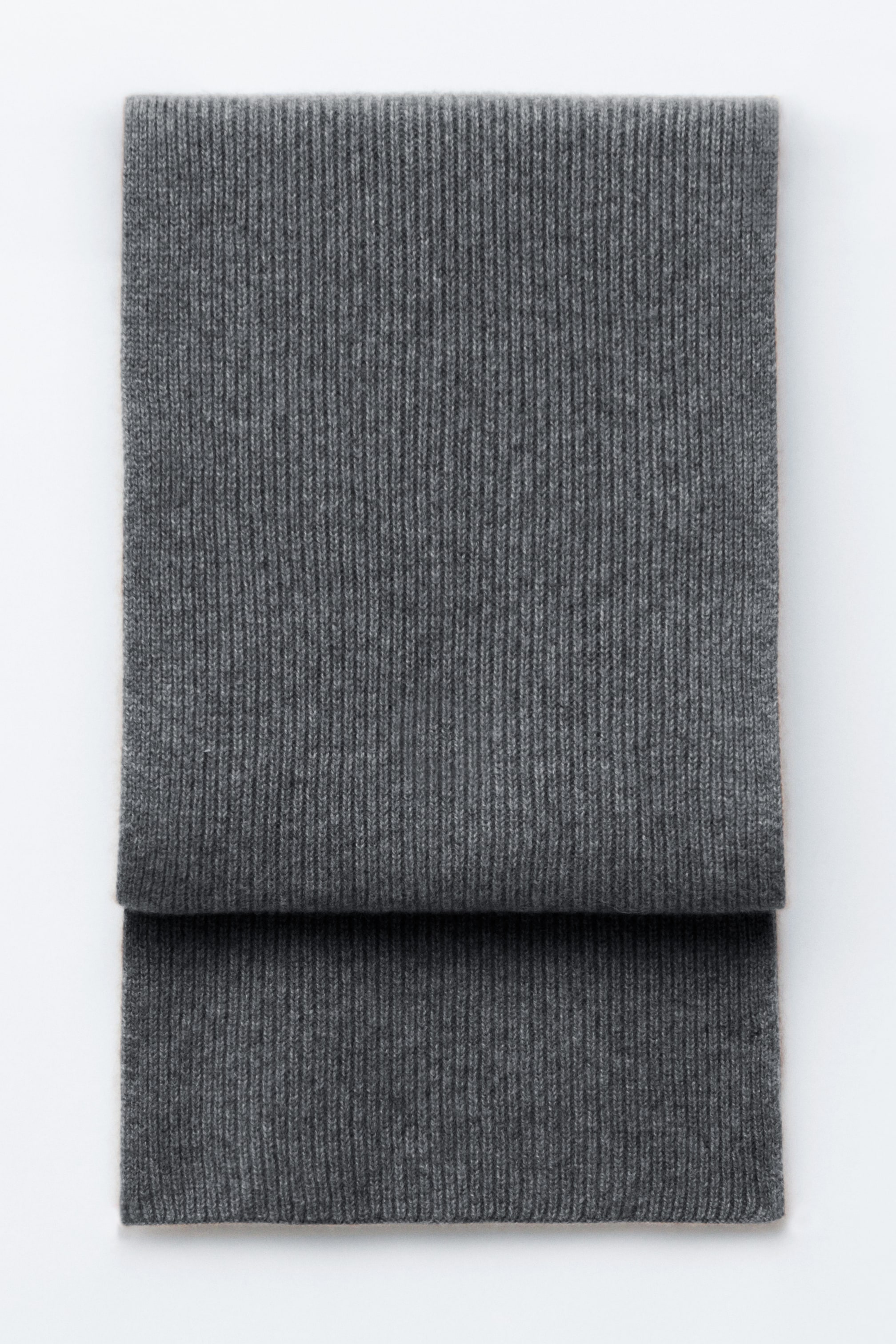View larger image: A dark grey knitted scarf featuring a vertical ribbed finish is lying folded flat, displaying its soft texture and rectangular design.