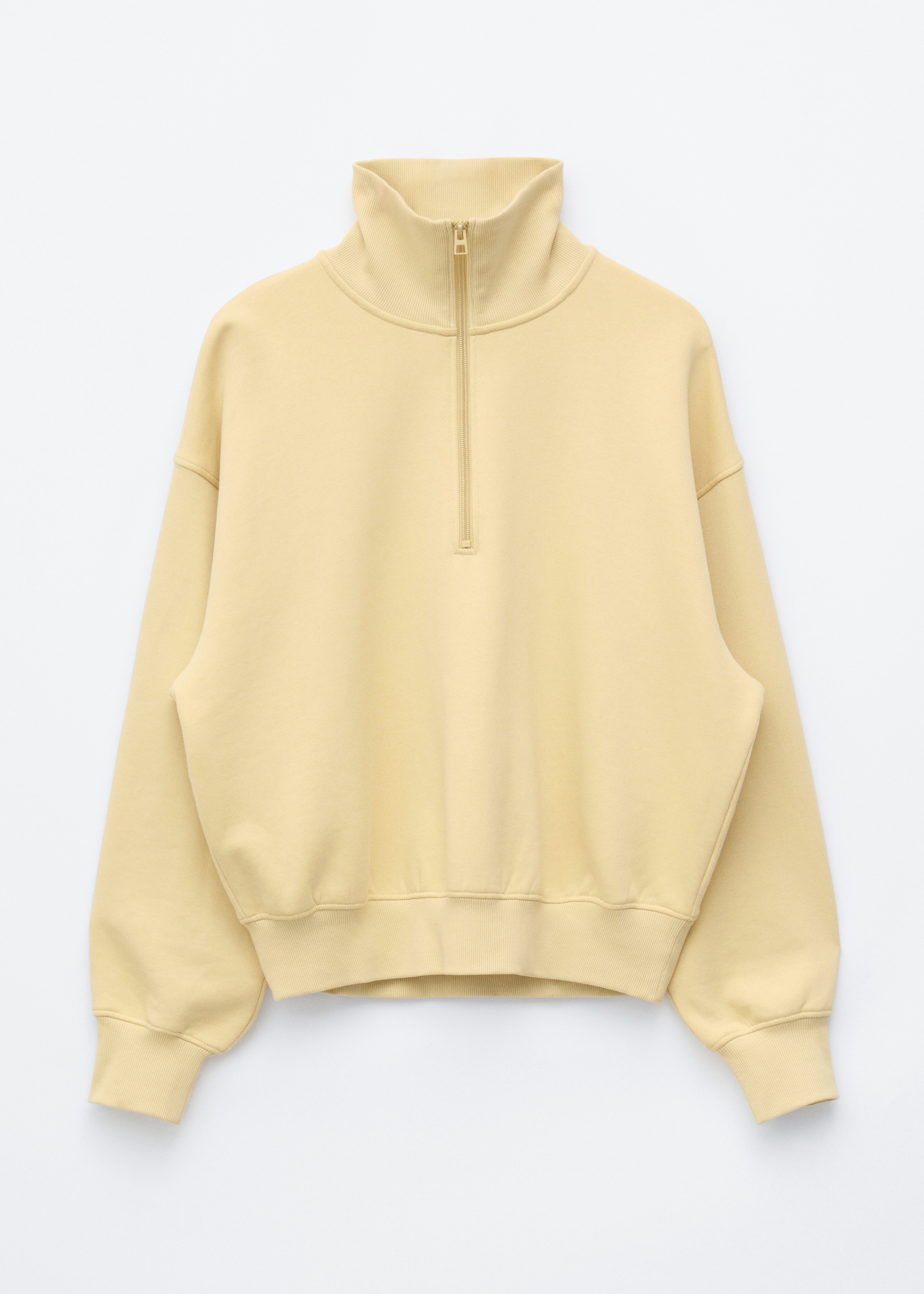 Un sweatshirt en jersey de coton jaune clair, dotÃ© dâune fermeture Ã  demi-zip et dâun col montant, est portÃ© par le modÃ¨le. Ce sweatshirt Ã  coupe dÃ©contractÃ©e prÃ©sente des Ã©paules tombantes avec des poignets cÃ´telÃ©s et est portÃ© en superposition sur un t-shirt blanc, rentrÃ© dans un pantalon noir.