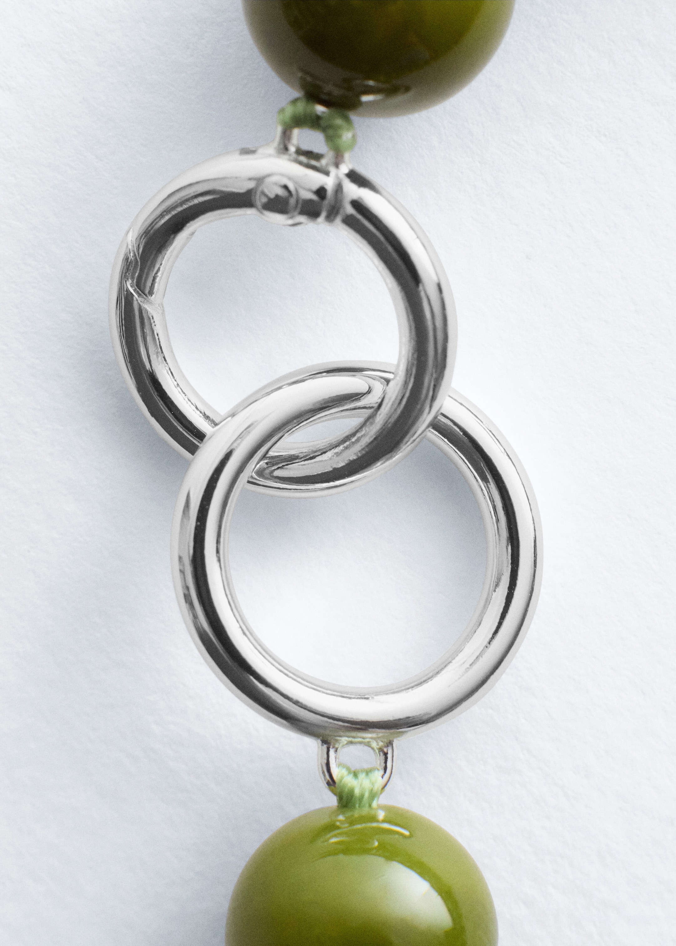 Grotere afbeelding bekijken: Een zilverkleurige O-ring sluiting wordt getoond, die twee ronde, glanzende, olijfgroene kralen verbindt. De sluiting bestaat uit twee in elkaar grijpende ringen; de bovenste ring heeft een veer-luik openingsmechanisme.