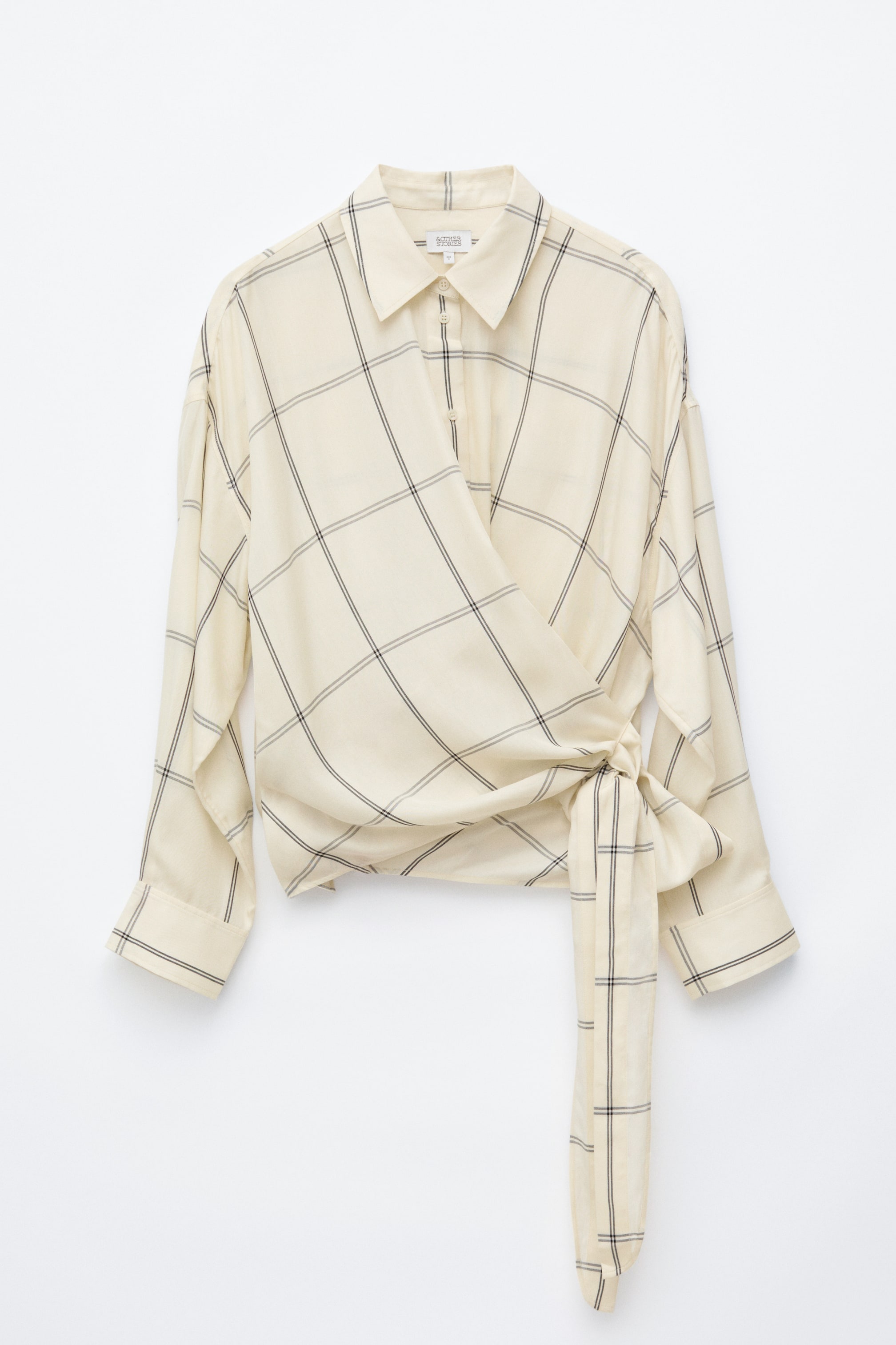 Grotere afbeelding bekijken: Een vooraanzicht van het Tie-Waist Cotton Shirt toont een offwhite stof met een zwart windowpane-ruitpatroon. Het shirt heeft een gedrapeerde overslag aan de voorkant die aan de zijkant van de taille wordt vastgemaakt met een lange strik in dezelfde stof, een klassieke puntkraag en lange mouwen met brede manchetten.