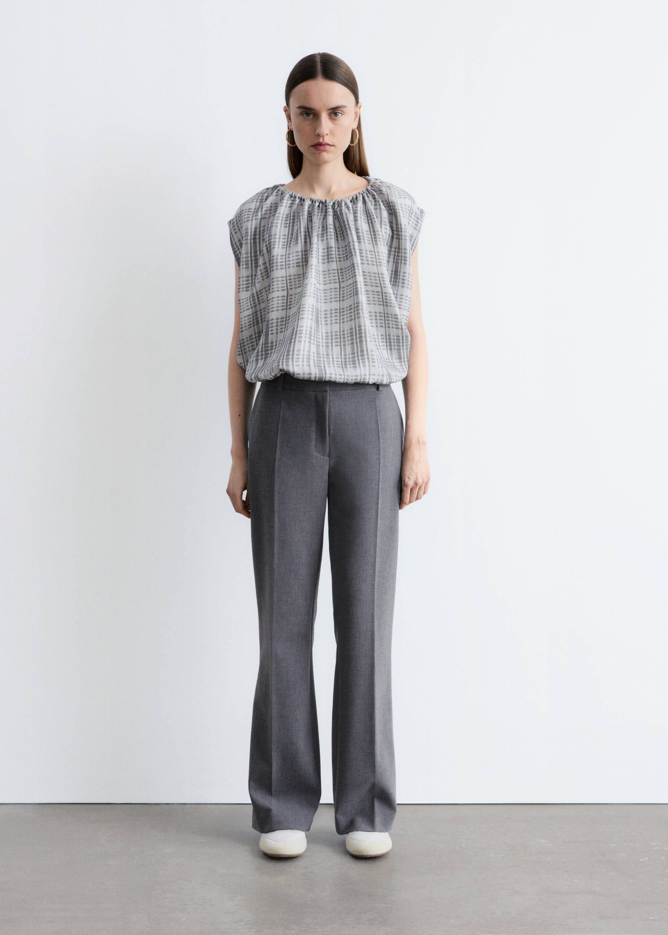 Ver imagen más grande: Un top con un patrón de cuadrícula de líneas finas en gris y blanco presenta un escote redondo fruncido y mangas cortas, con el dobladillo fruncido metido en unos pantalones anchos de pierna en gris oscuro. Los pantalones muestran una prominente raya frontal que se extiende por cada pierna.