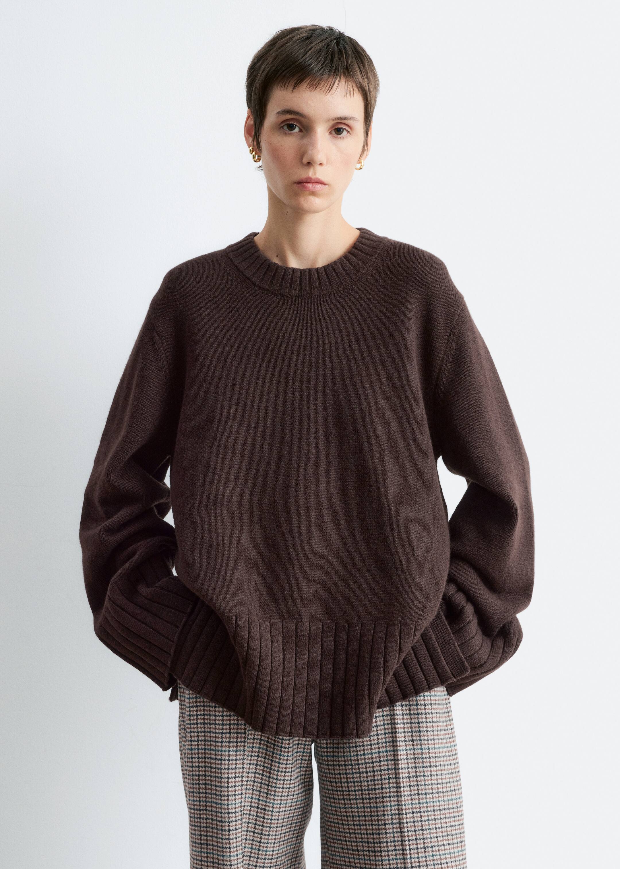 View larger image: A dark brown, soft-textured sweater is being presented, featuring a ribbed crew neck and long, loose-fitting sleeves. It is showcasing wide ribbed cuffs and a wide ribbed hem with a subtle side split, highlighting its relaxed fit.