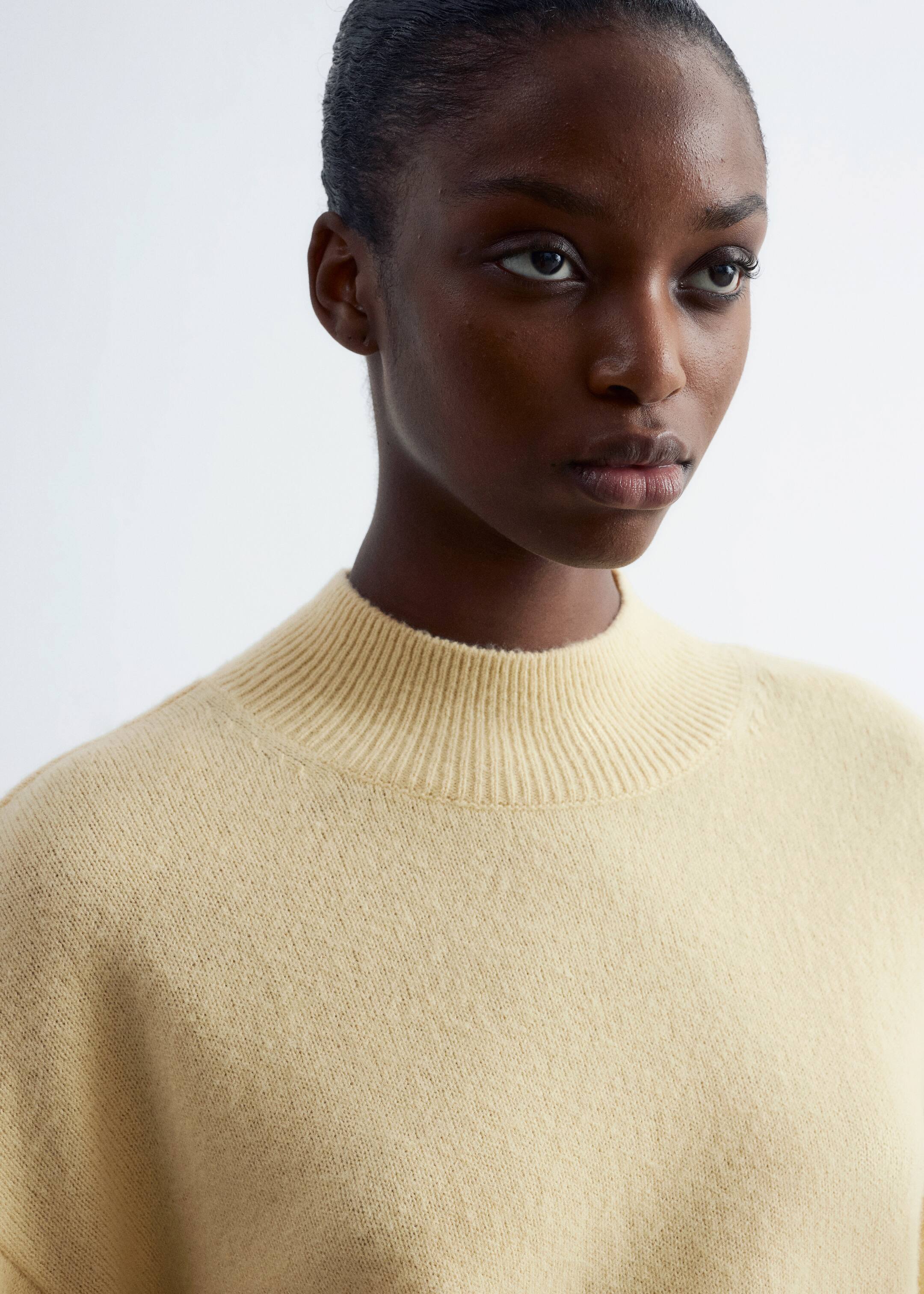 Agrandir l'image: Un pull jaune pâle est porté, avec un col montant côtelé et une texture douce et fine. Le vêtement présente une coupe décontractée au niveau de la poitrine et des épaules, vu sous un léger angle.