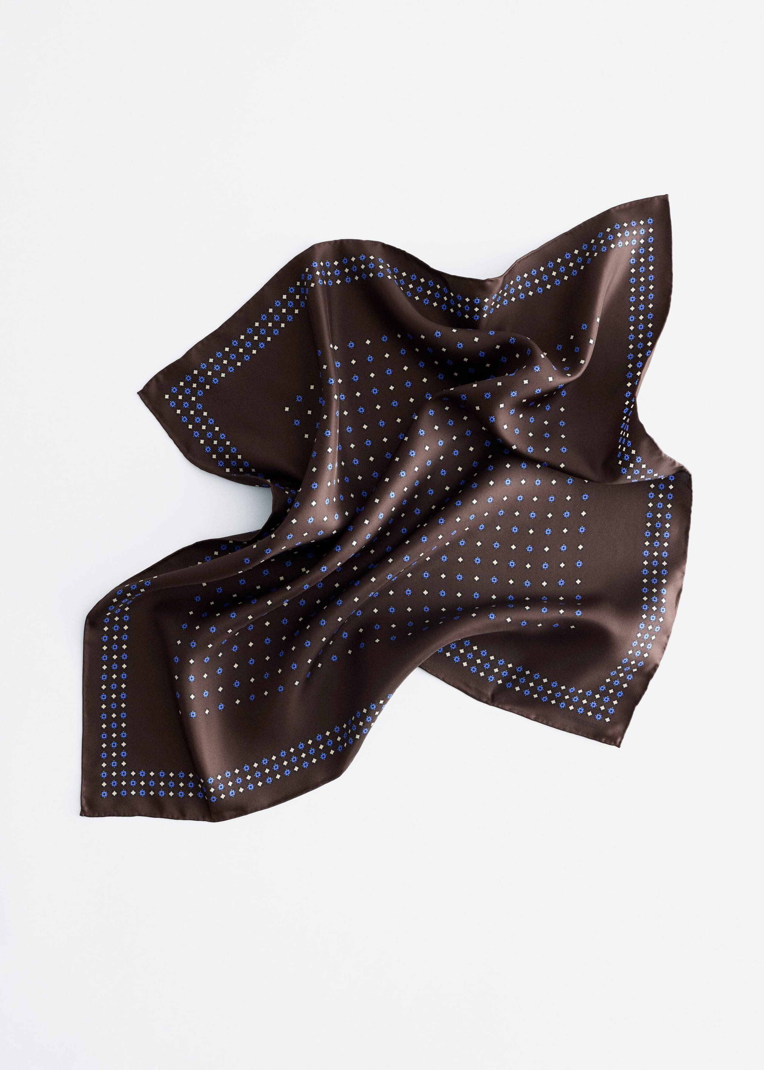 A square silk scarf in dark brown displays a lustrous sheen as it lies in an artfully draped, folded arrangement. It features an all-over pattern of small blue and white geometric motifs, with a decorative double-row border along the edges.