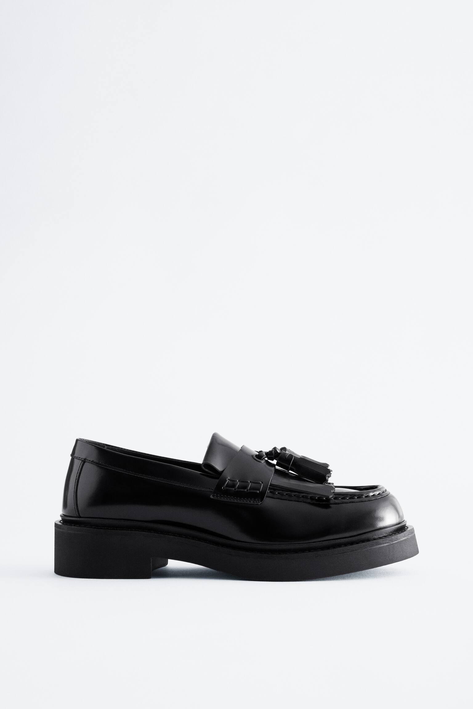 Un loafer din piele neagrÄ lustruitÄ este aÈezat Ã®ntr-o vedere din profil lateral, evidenÈiind o talpÄ neagrÄ masivÄ Èi un toc jos, drept. Pantoful prezintÄ ciucuri decorativi Èi un detaliu franjurat kiltie peste carÃ¢mb, alÄturi de cusÄturi moc-toe vizibile. - 1