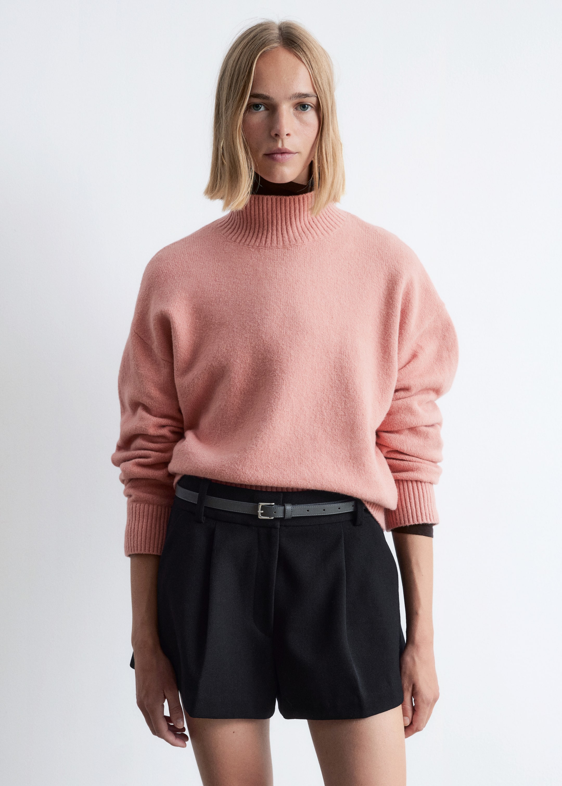 Größeres Bild anzeigen: Ein weicher, flauschiger Strickpullover in Rosa wird von vorne präsentiert und zeigt eine lockere Passform mit einem hohen, gerippten Stehkragen und langen Ärmeln mit gerippten Bündchen. Er wird über einem dunklen, hochgeschlossenen Oberteil getragen.