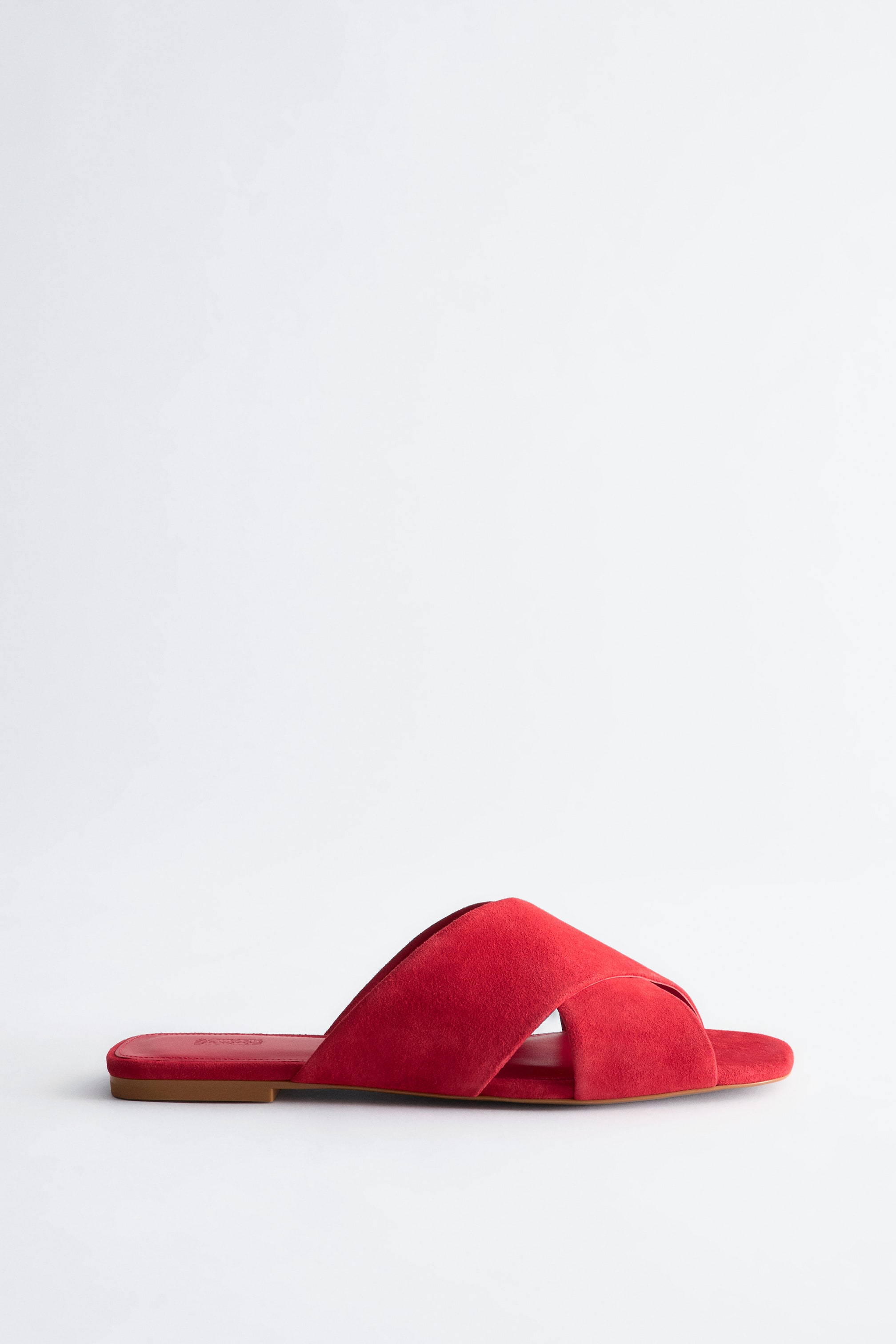 Visualizza immagine più grande: Un sandalo a ciabatta in pelle scamosciata rossa presenta ampi cinturini incrociati che formano una forma a X sopra il plantare, con il profilo sinistro che rivela una sottile suola marrone.