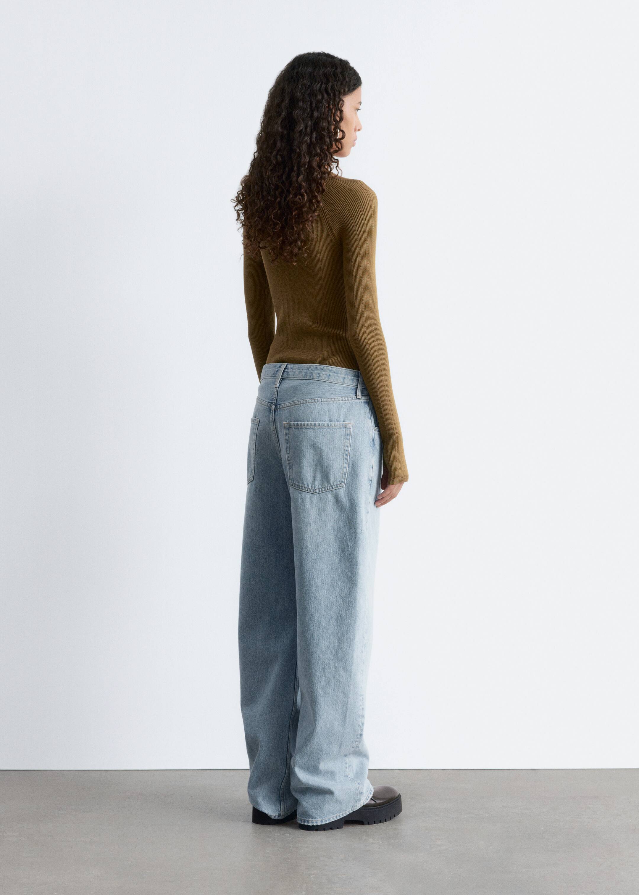 Größeres Bild anzeigen: Die in Slim-Fit geschnittene, olivgrüne Rippstrick-Bodysuit mit langen Raglanärmeln und Daumenlöchern wird vom Model getragen, das dazu eine hellblaue, weit geschnittene Jeans trägt.
