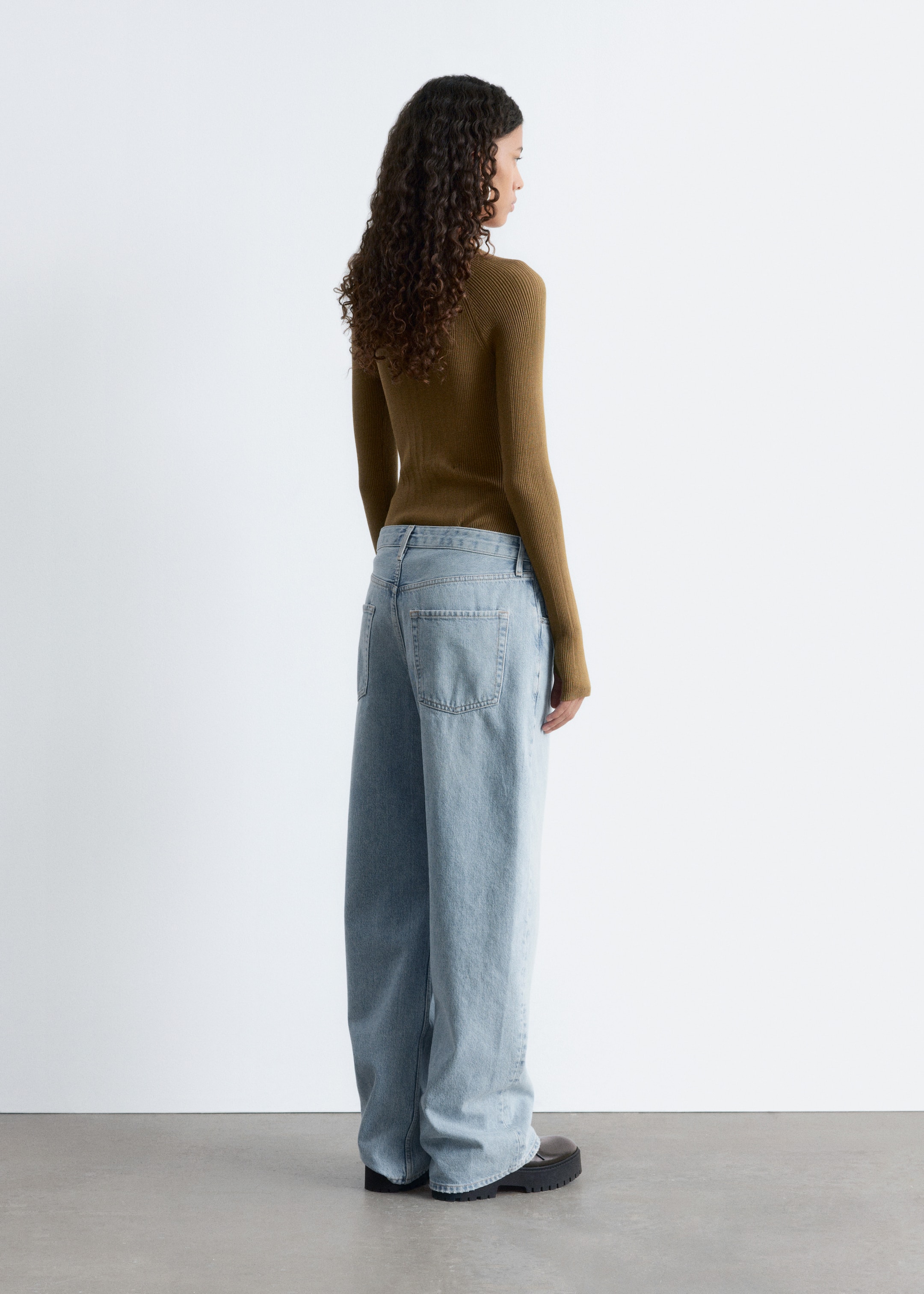 View larger image: A slim-fit olive green rib-knit bodysuit, featuring long raglan sleeves with thumbhole openings, is being worn by the model, who is also wearing light blue wide-leg jeans.