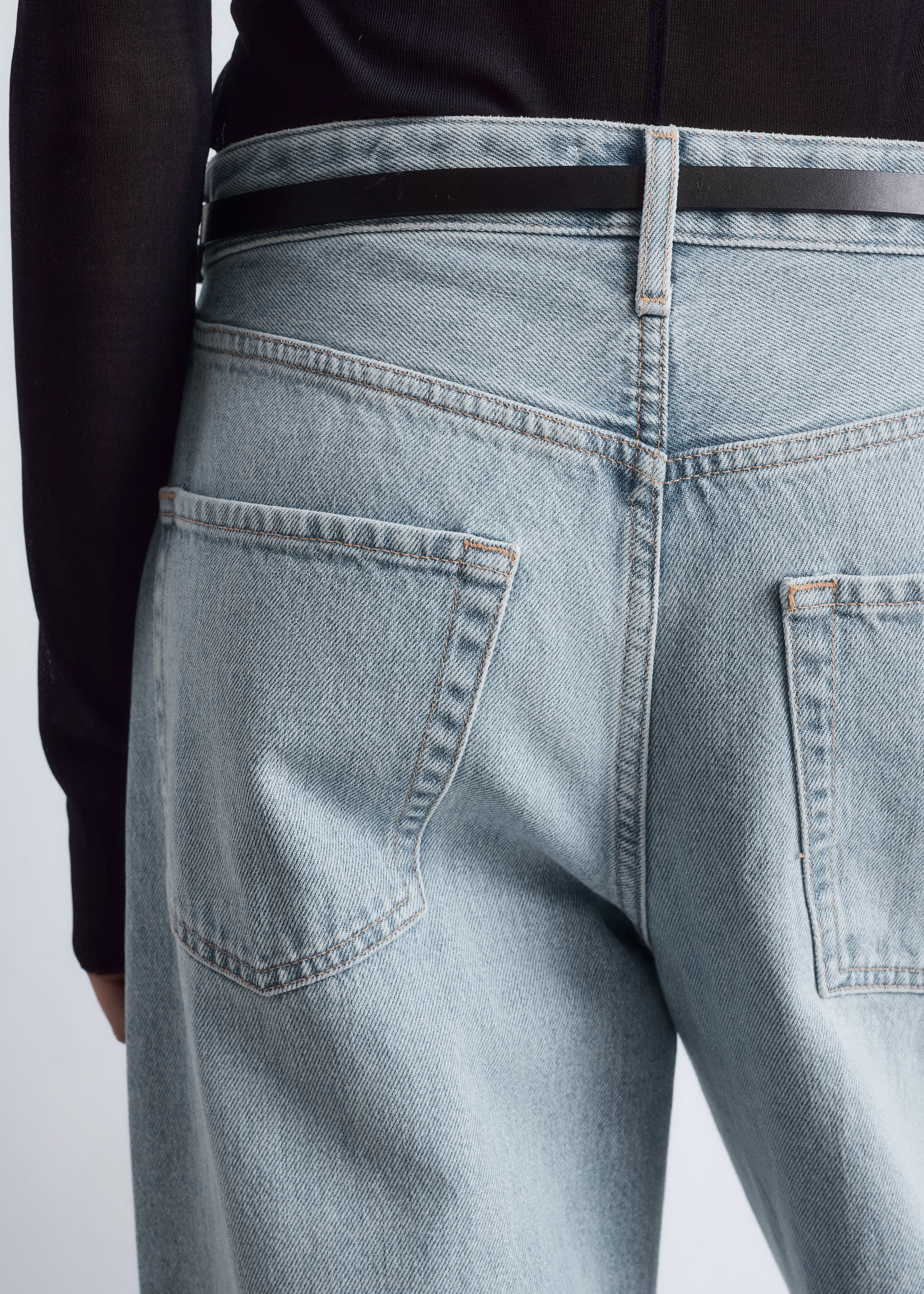 Agrandir l'image: Un jean bleu clair est présenté de dos, avec une coupe décontractée, des surpiqûres contrastantes orange et deux poches plaquées à l'arrière, accompagné d'une fine ceinture noire passée dans les passants de ceinture.