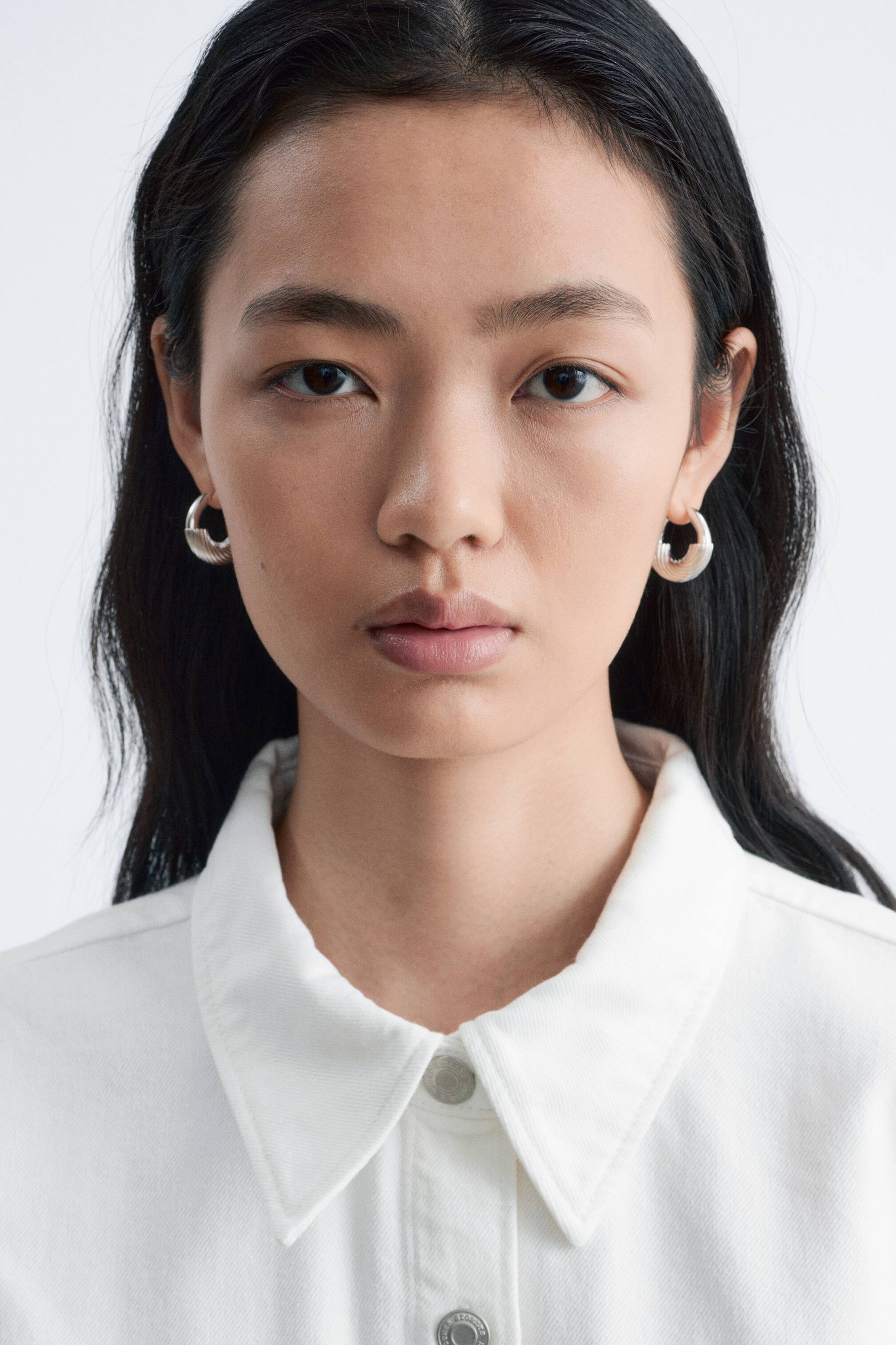 Se større billede: Sølvfarvede hoop-øreringe med rillet tekstur bæres af modellen.