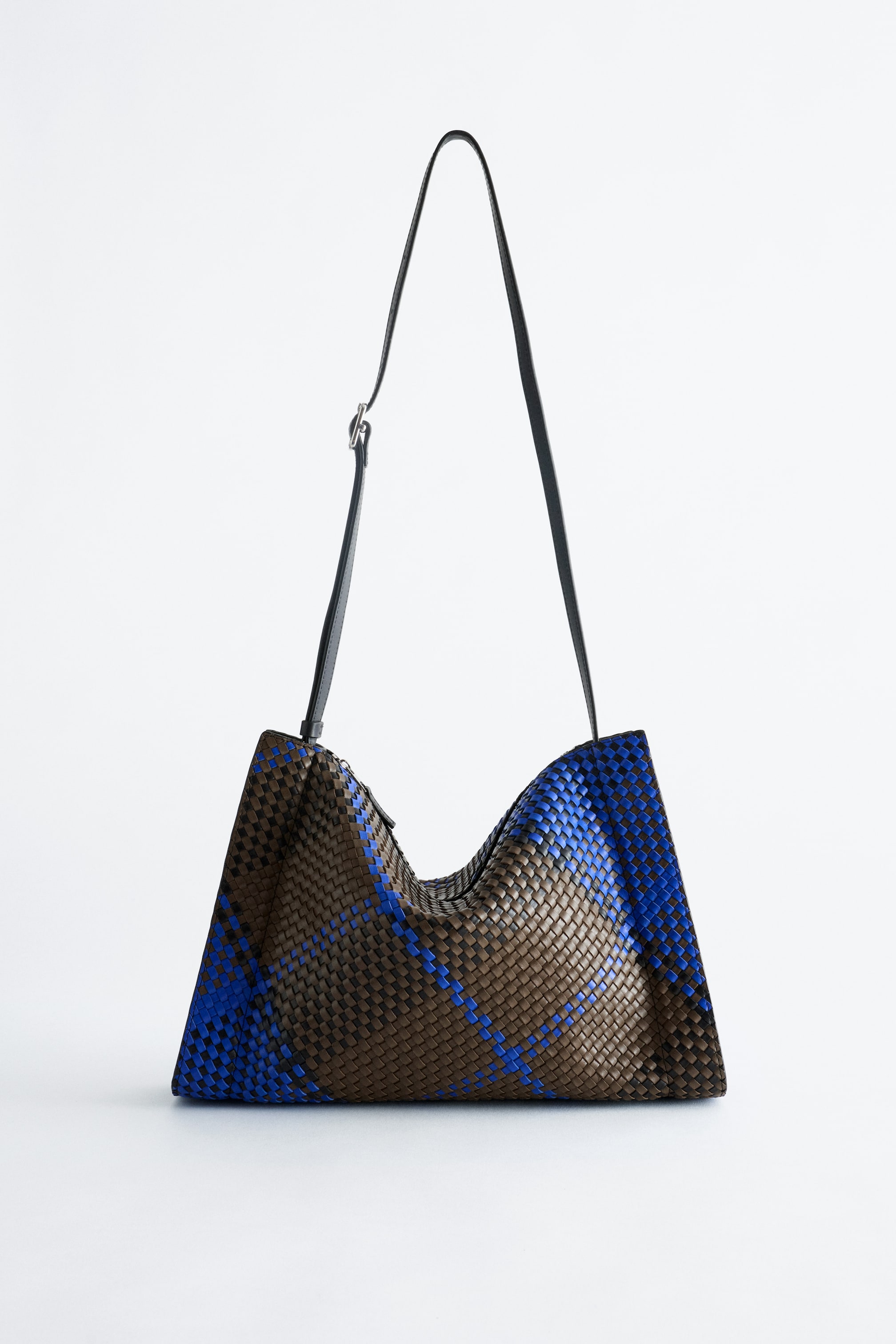 Agrandir l'image: Un sac à main tissé est suspendu, face à l’avant, mettant en valeur son corps avec une base marron et des rayures diagonales bleues et noires qui se croisent, ainsi que sa structure souple et décontractée. Il est doté d’une bandoulière noire réglable.