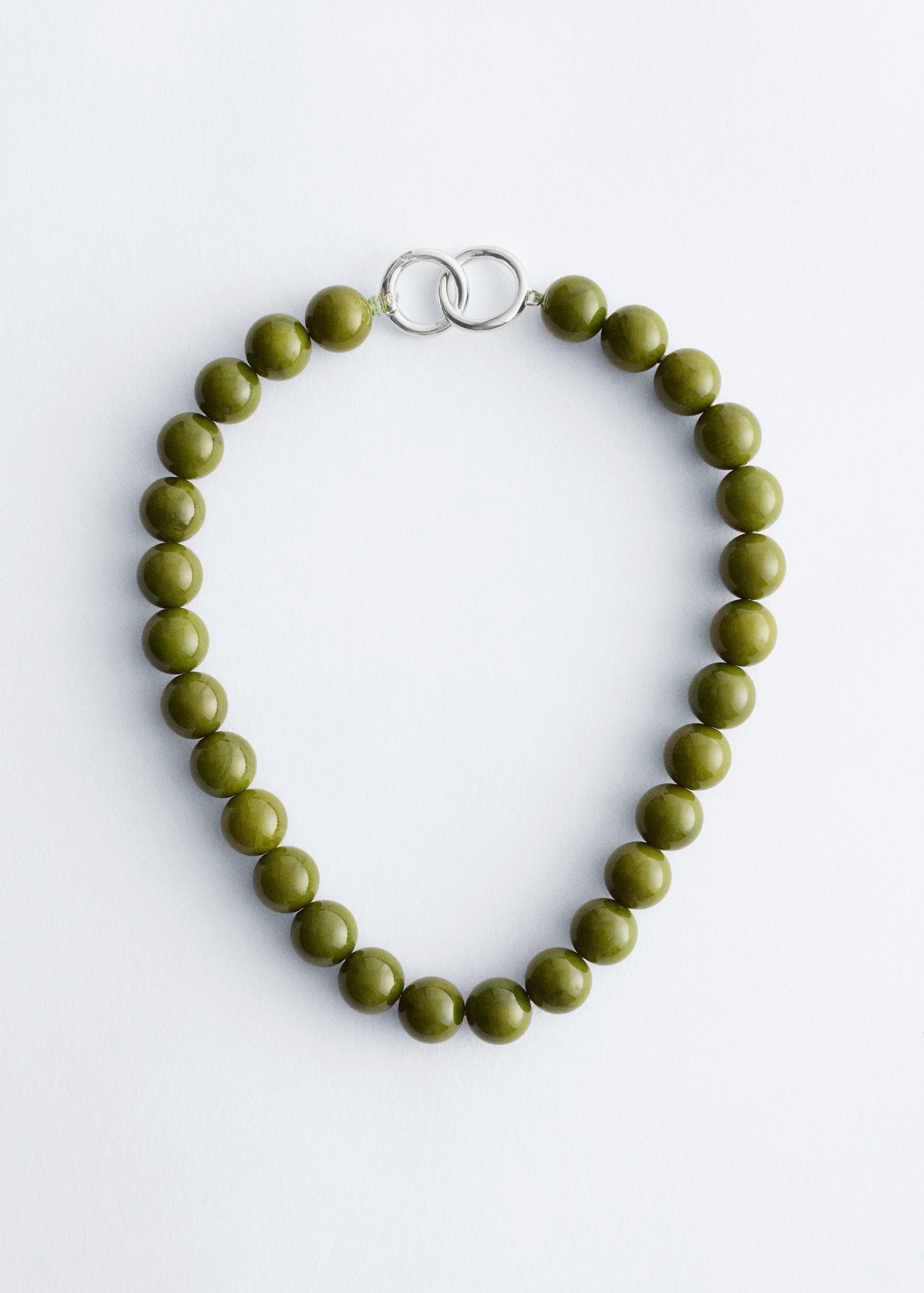 Grotere afbeelding bekijken: Een stenen kralenketting met ronde, olijfgroene kralen wordt gepresenteerd vanaf de VOORKANT. Een delicate, zilverkleurige O-ring sluiting verbindt de uiteinden van de kralenstreng.
