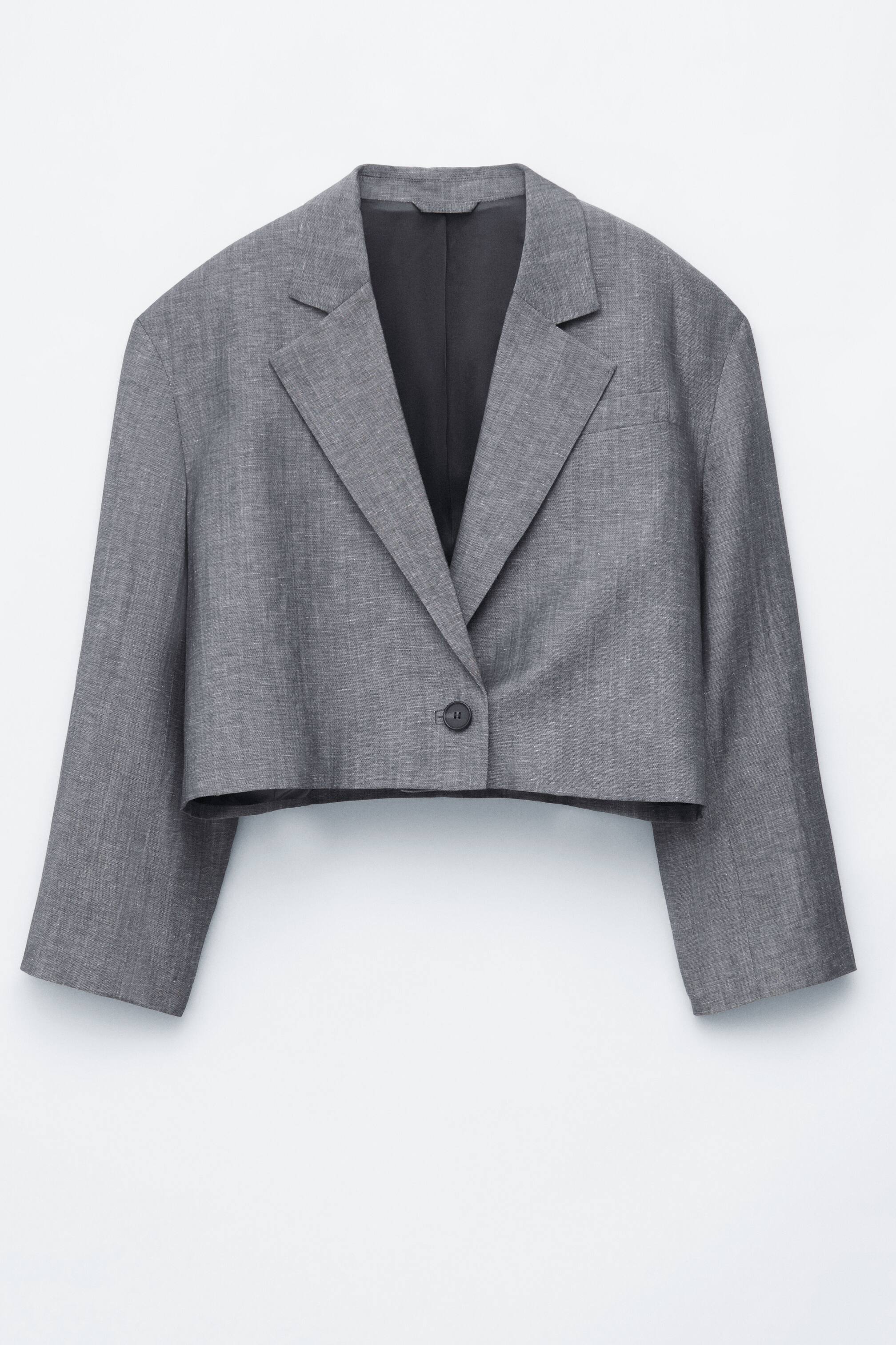 Grotere afbeelding bekijken: Een grijze blazer met textuur en een cropped model wordt gepresenteerd, voorzien van notch revers en een enkele knoopsluiting. Het is ontworpen met lange mouwen, een cropped zoom en een zichtbare donkere voering.