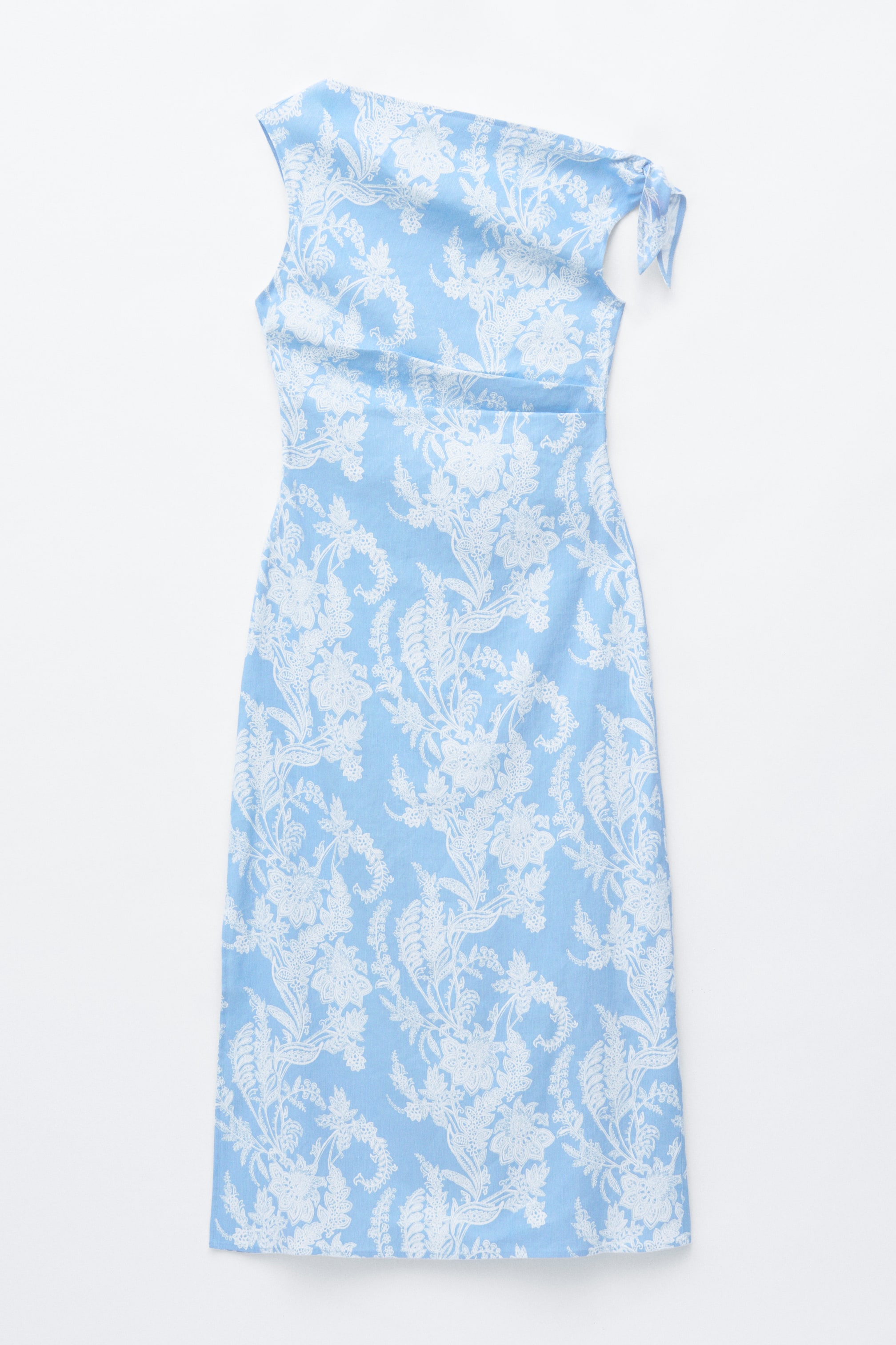 Visa större bild: En midiklänning visas framifrån, med ett ljusblått tyg med ett vitt paisleymönster. Den är designad med en asymmetrisk halsringning, ett justerbart avtagbart axelband på ena sidan och veck som formar midjan.