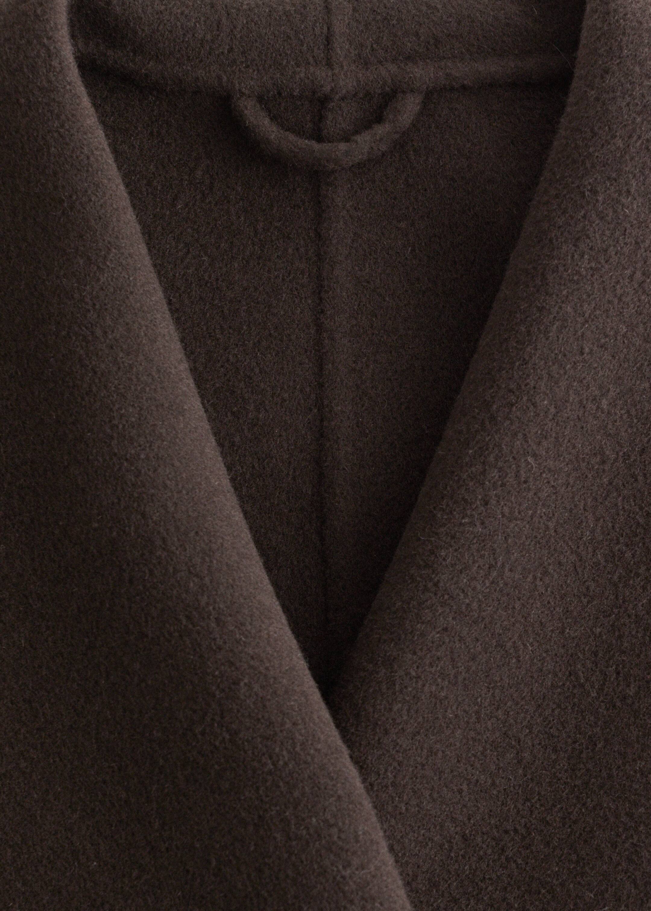 Visualizza immagine più grande: Il cappotto in misto lana marrone scuro viene mostrato in una vista ravvicinata, mettendo in risalto la sua texture morbida e pelosa. Il suo ampio colletto a scialle forma una profonda forma a V sul davanti, e un piccolo anello per appenderlo è visibile sul retro del collo.