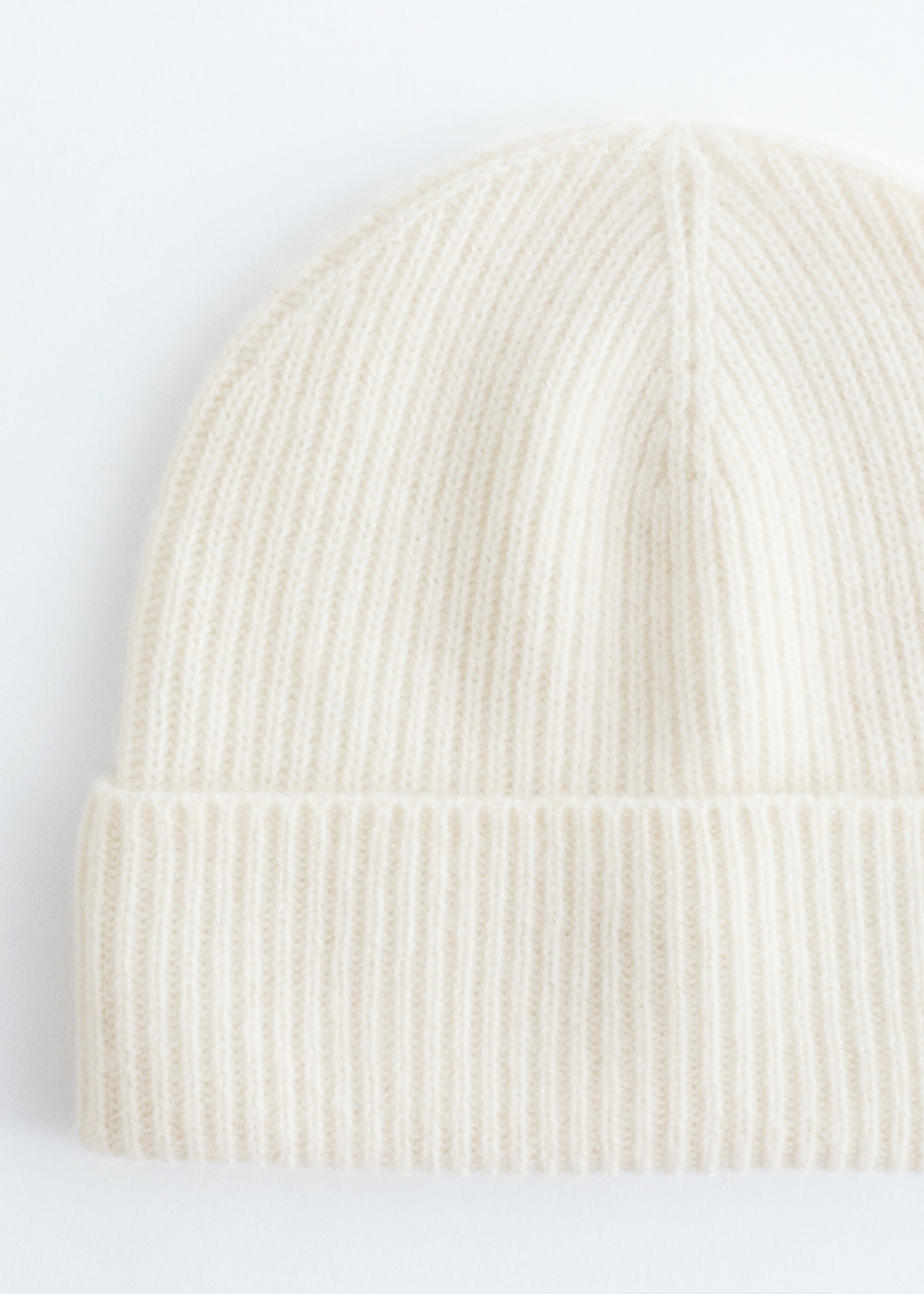 Größeres Bild anzeigen: Eine cremeweiße Mütze aus reinem Kaschmir wird von vorne gezeigt, mit einem gerippten Strickmuster und einem breiten Umschlagbund.