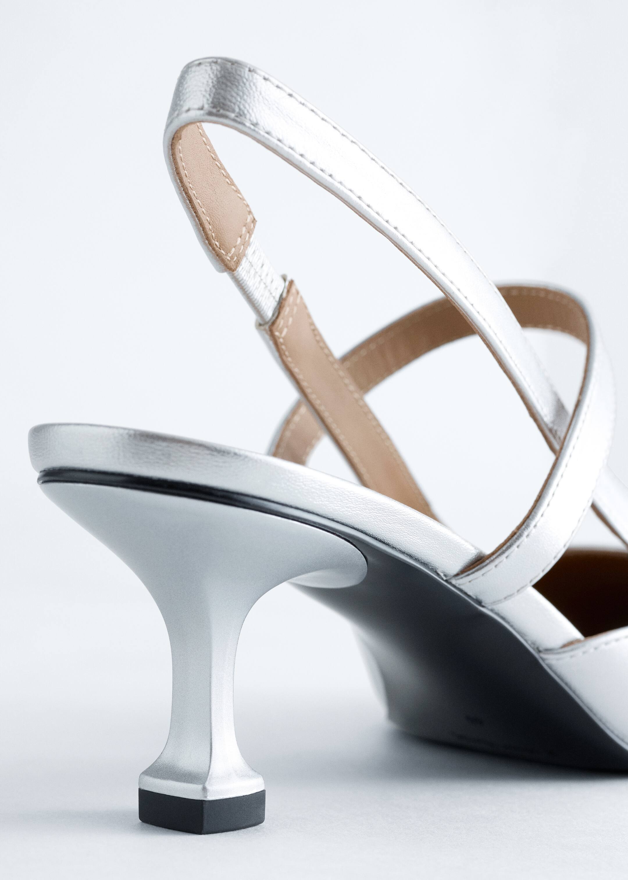 Agrandir l'image: Une chaussure slingback argentée métallique est présentée de dos, avec une fine bride slingback argentée dotée d'un insert élastique beige et un talon kitten évasé argenté avec une pointe noire.