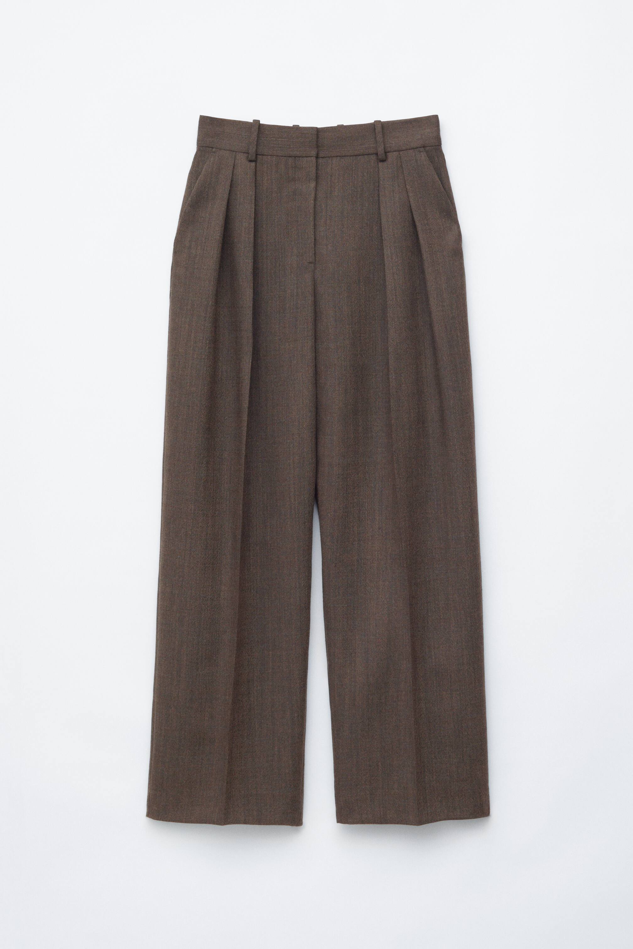 Ver imagen más grande: Los pantalones marrones se presentan desde el frente, con una cinturilla que incluye trabillas para cinturón y un cierre de botón en la parte superior. Están diseñados con pliegues dobles en el frente, bolsillos laterales inclinados y piernas anchas que muestran marcadas líneas de planchado.