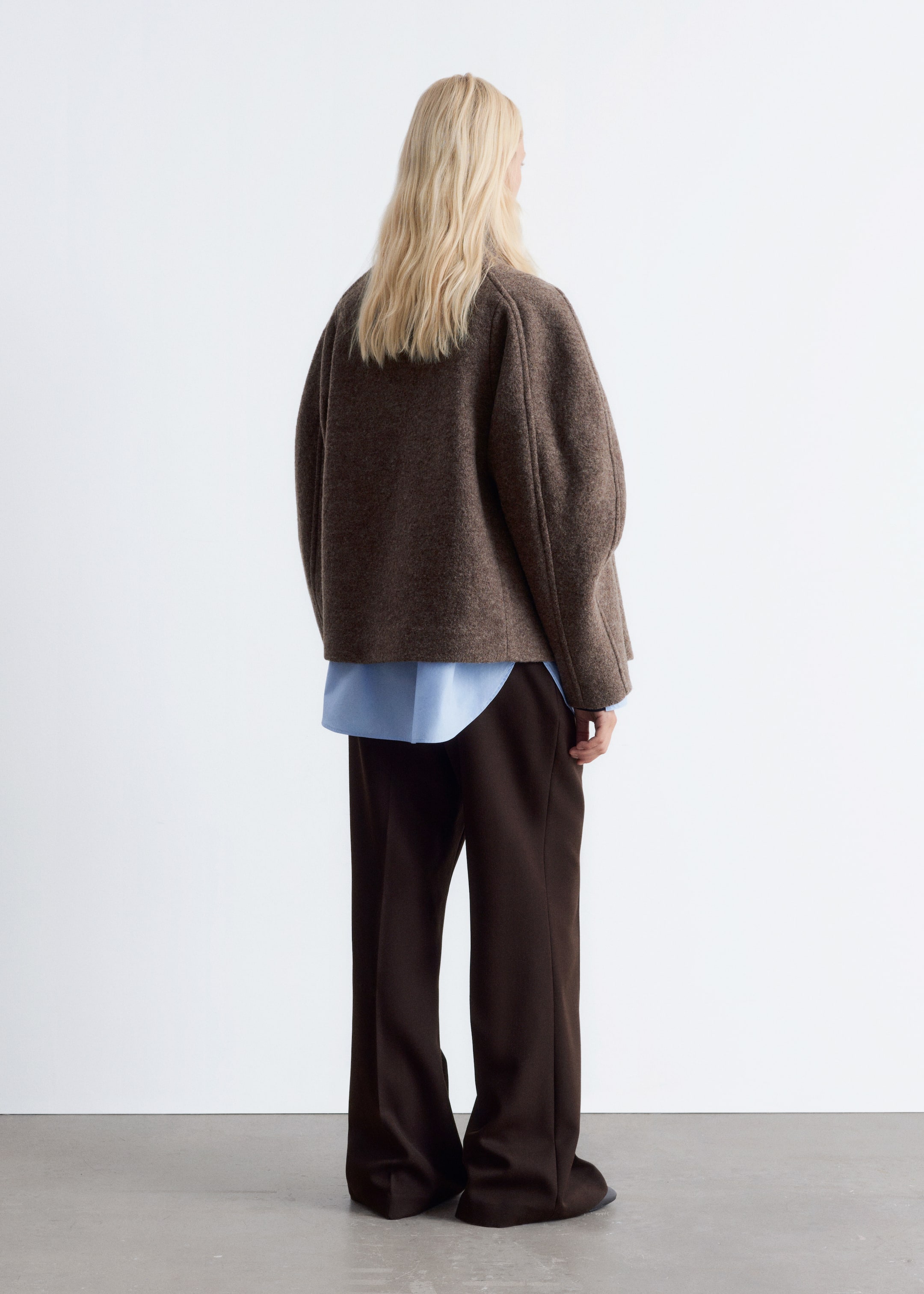 View larger image: A brown wool jacket with a short, boxy silhouette and wide sleeves is being worn by the model. It is worn over a light blue shirt and paired with dark brown wide-leg trousers.